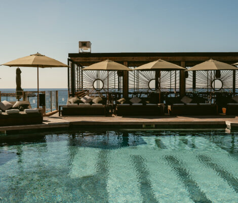 Het zwembad met day beds en parasols van UM Beach House met de zee erachter bij Puerto Portals