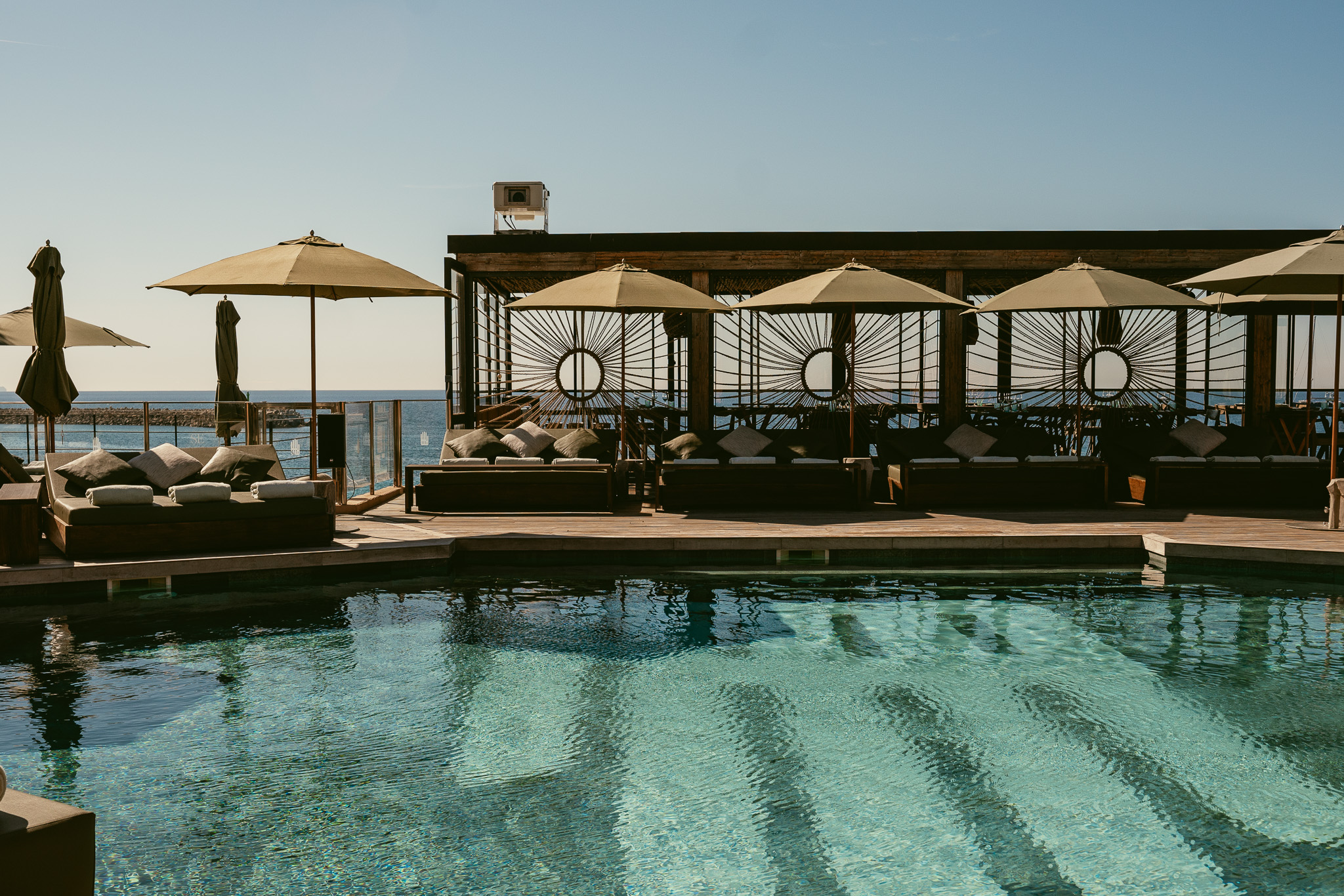 Het zwembad met day beds en parasols van UM Beach House met de zee erachter bij Puerto Portals