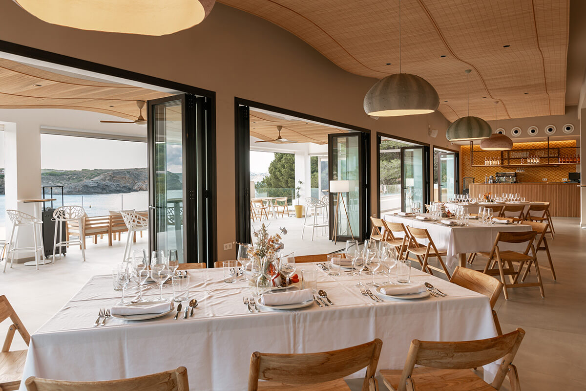 De eetzaal met gedekte tafels en zeezicht van Viva La Pepa op Menorca