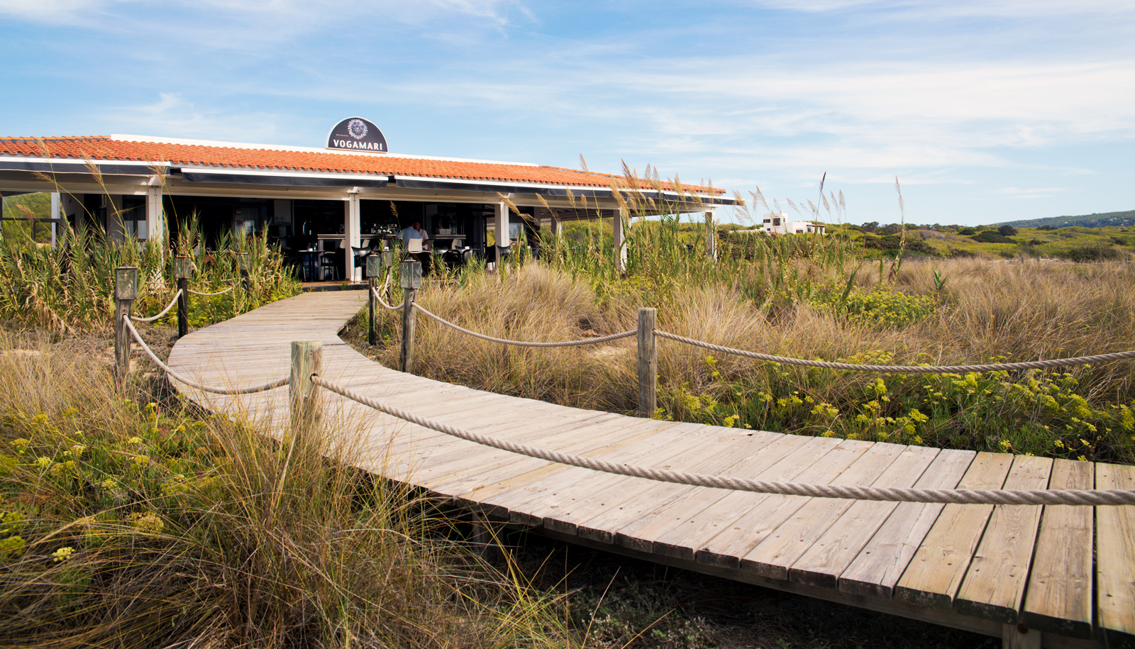Het strandrestaurant Vogamarí aan Platja de Migjorn, met een houten pad door de duinen naar de zee