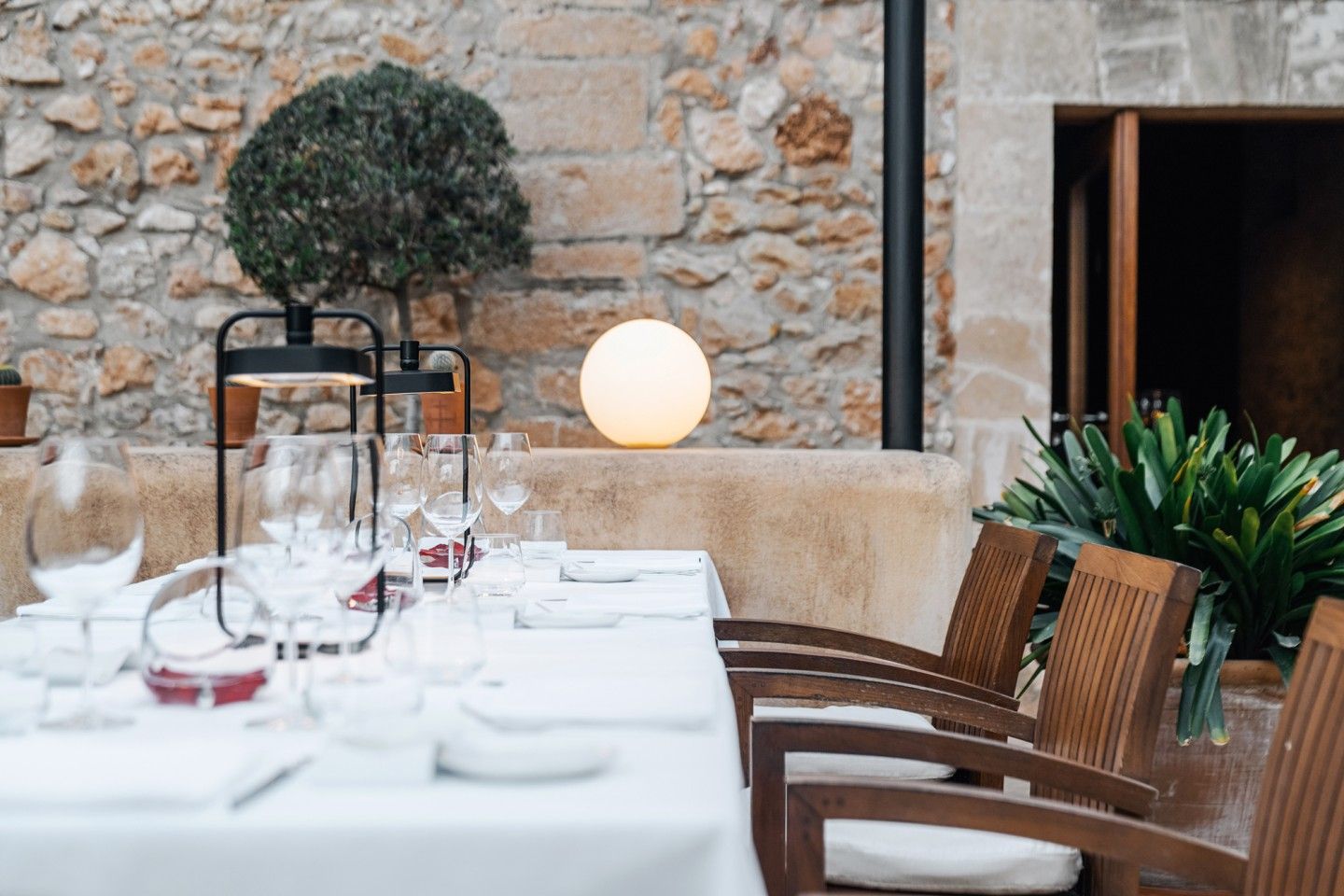 365 bij Son Brull (Pollença): het menu uit de eigen finca 3 Gedekte tafel op het terras van Son Brull met glazen, een bolvormige lamp en de natuurstenen gevel erachter