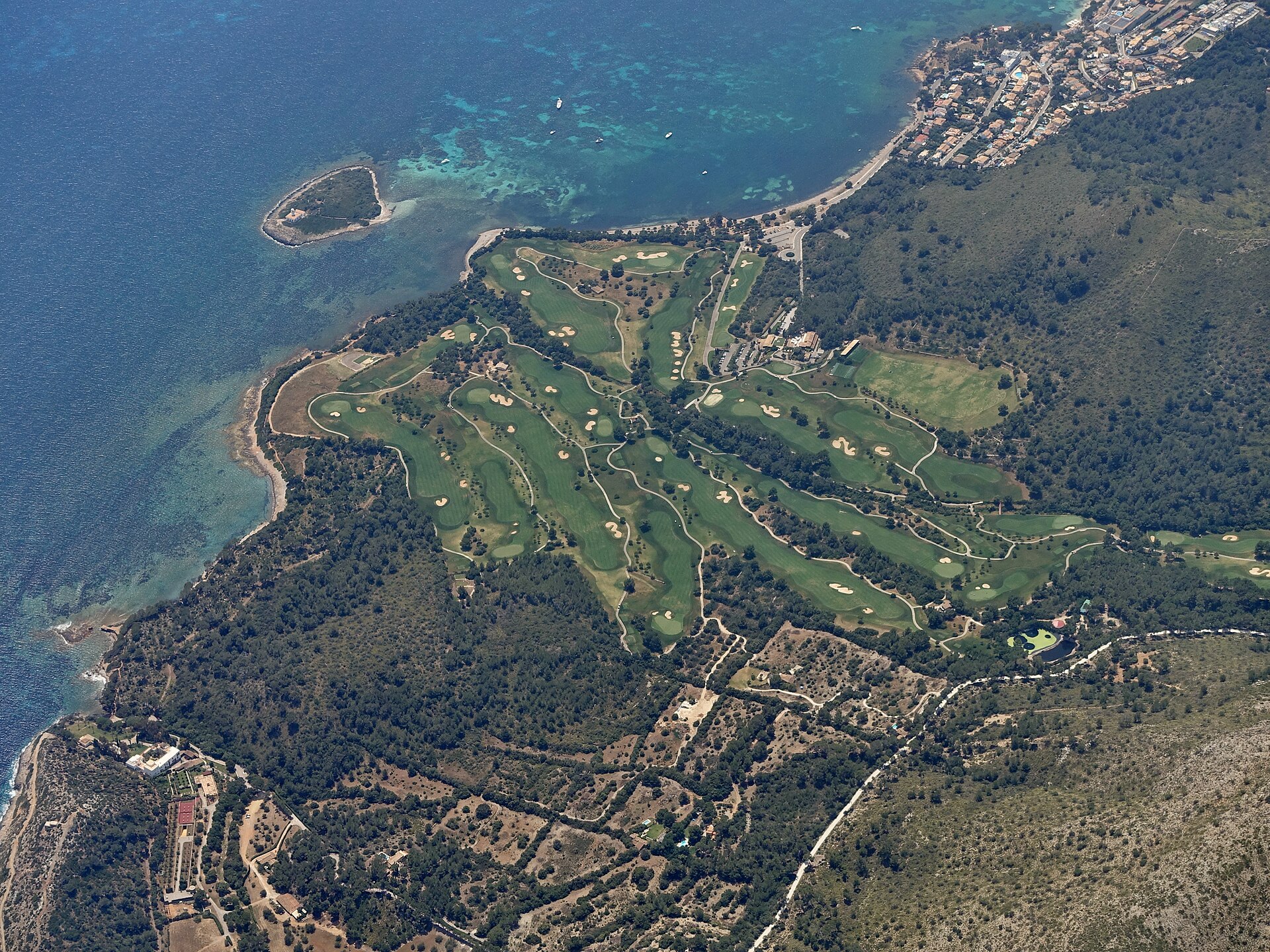 Alcanada Mallorca: rustig snorkelstrand met vuurtoreneilandje 6 Luchtfoto van Alcanada met het vuurtoreneilandje voor de kust en de groene fairways van de golfbaan erachter
