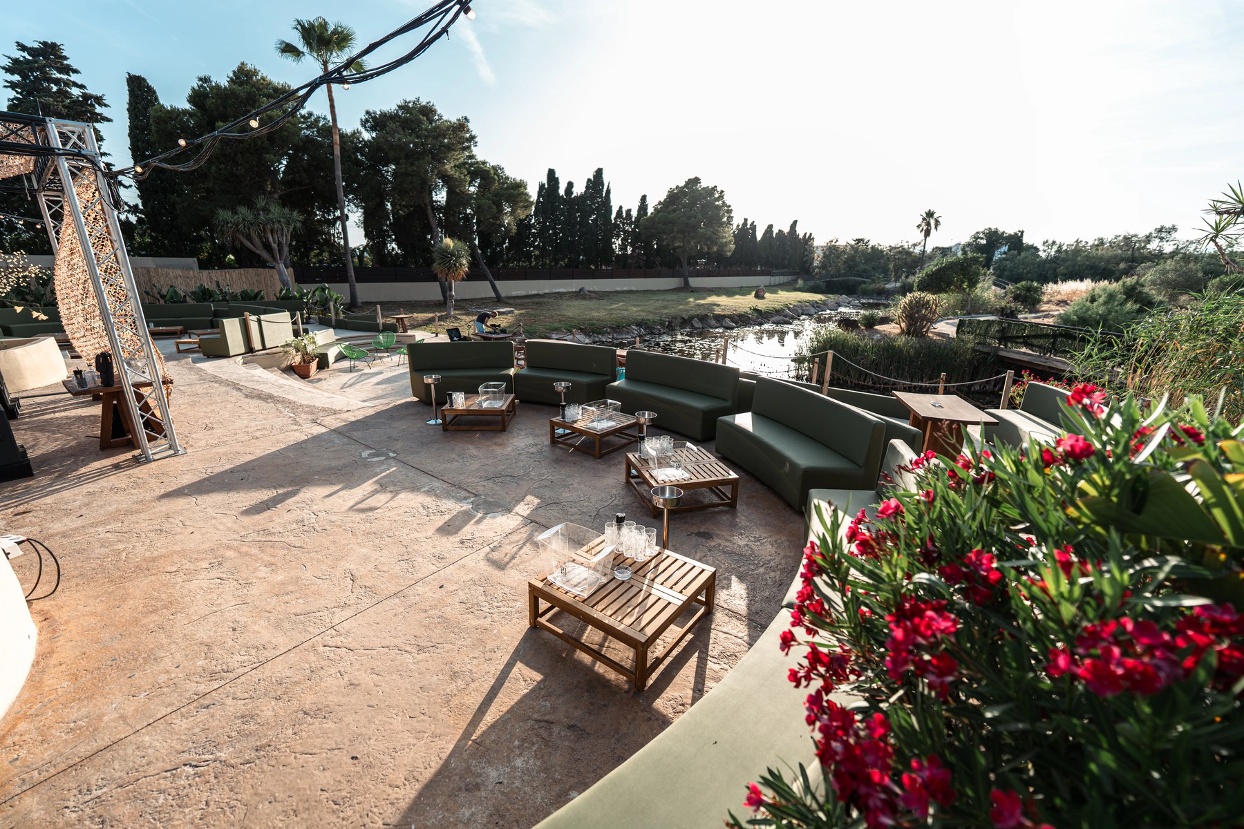 Het openluchtterras van Amok Mallorca met groene ronde banken, houten tafels en de vijver erachter