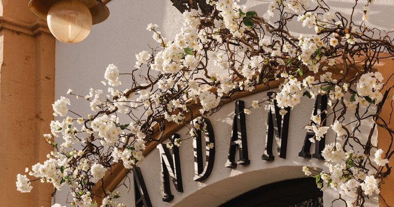 De gevel van restaurant Andana in Palma met de naam in zwarte letters boven de boogdeur en witte bloesemtakken om de lantaarn