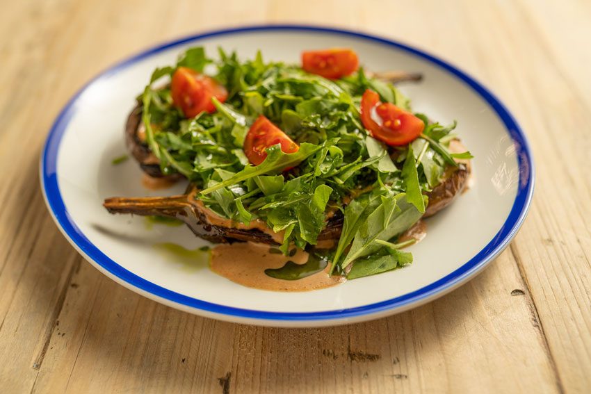 Andana Palma: eten in het eerste treinstation van Mallorca 5 Langzaam geroosterde aubergine met rucola en tomaat op een bord met blauwe rand bij Andana in Palma