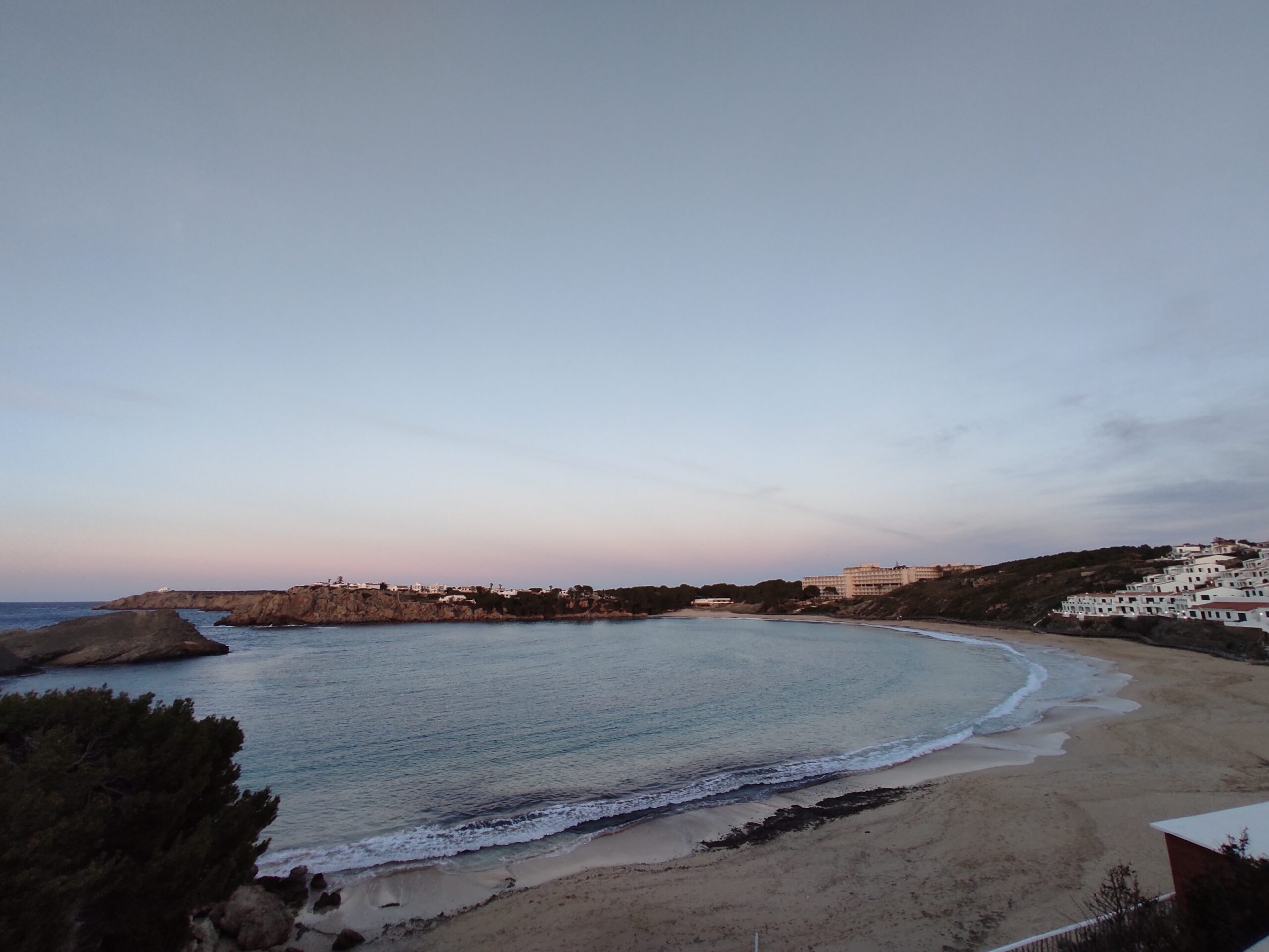 Het lege strand van Arenal d'en Castell in de schemering met de hoefijzervorm van de baai