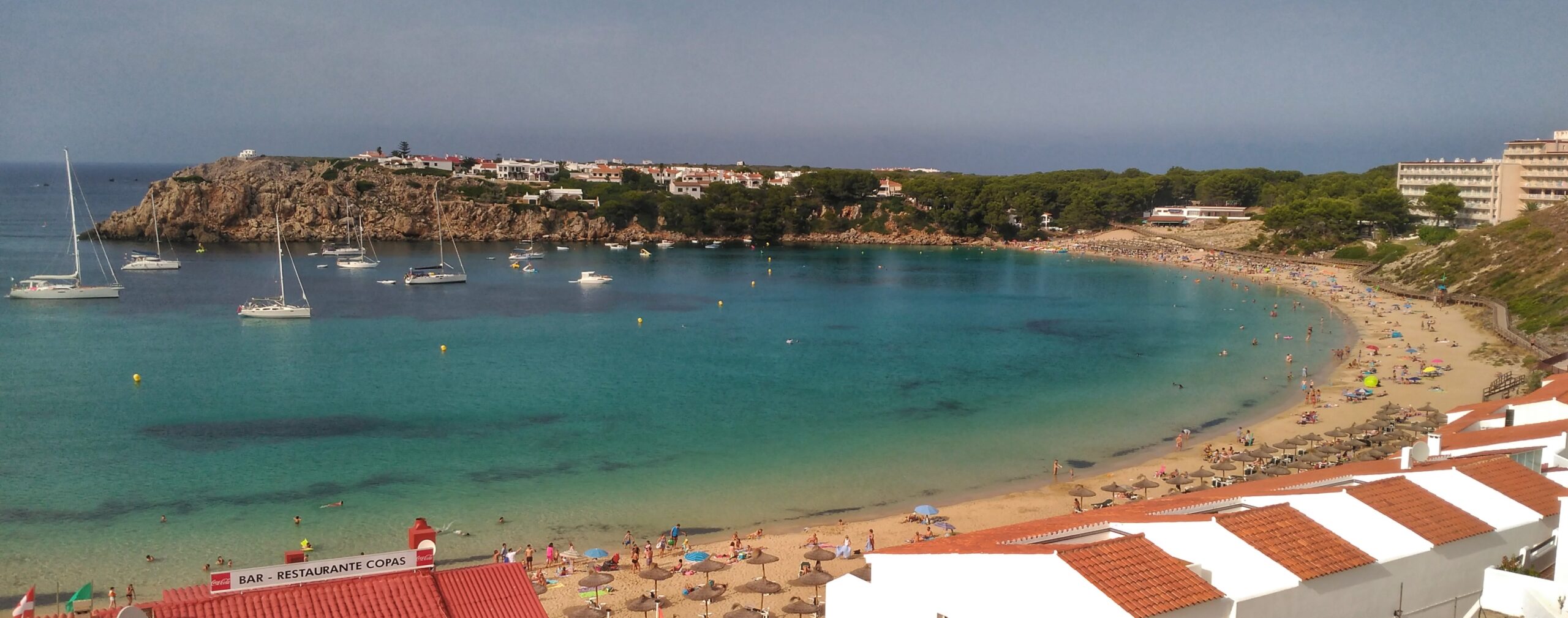 De bijna ronde baai van Arenal d'en Castell op Menorca met zeilboten voor anker en de zandboog aan de rechterkant