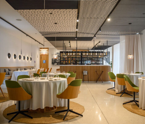 De eetzaal van restaurant Aromata in Palma met ronde tafels, groene en oranje stoelen en op de achtergrond de bar met wijnrekken