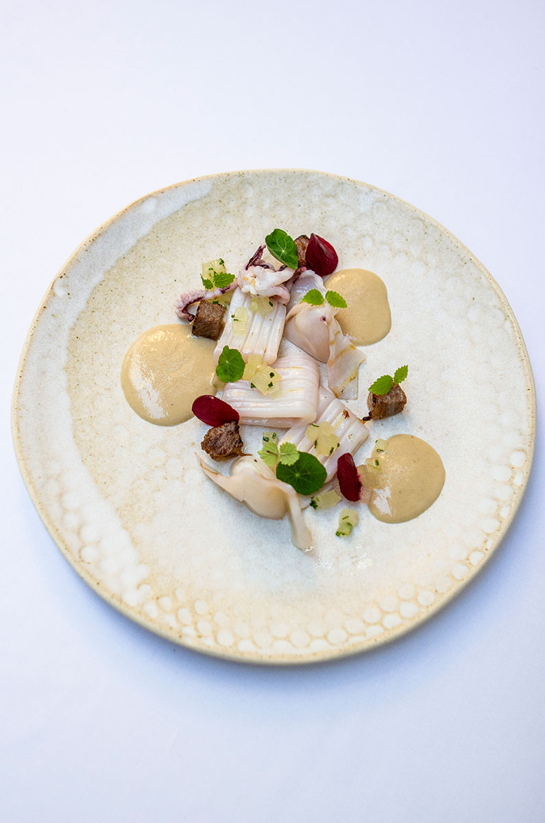 Bord van Aromata met witte asperge, blaadjes en puntjes saus op een lichtgroen glazuurd bord