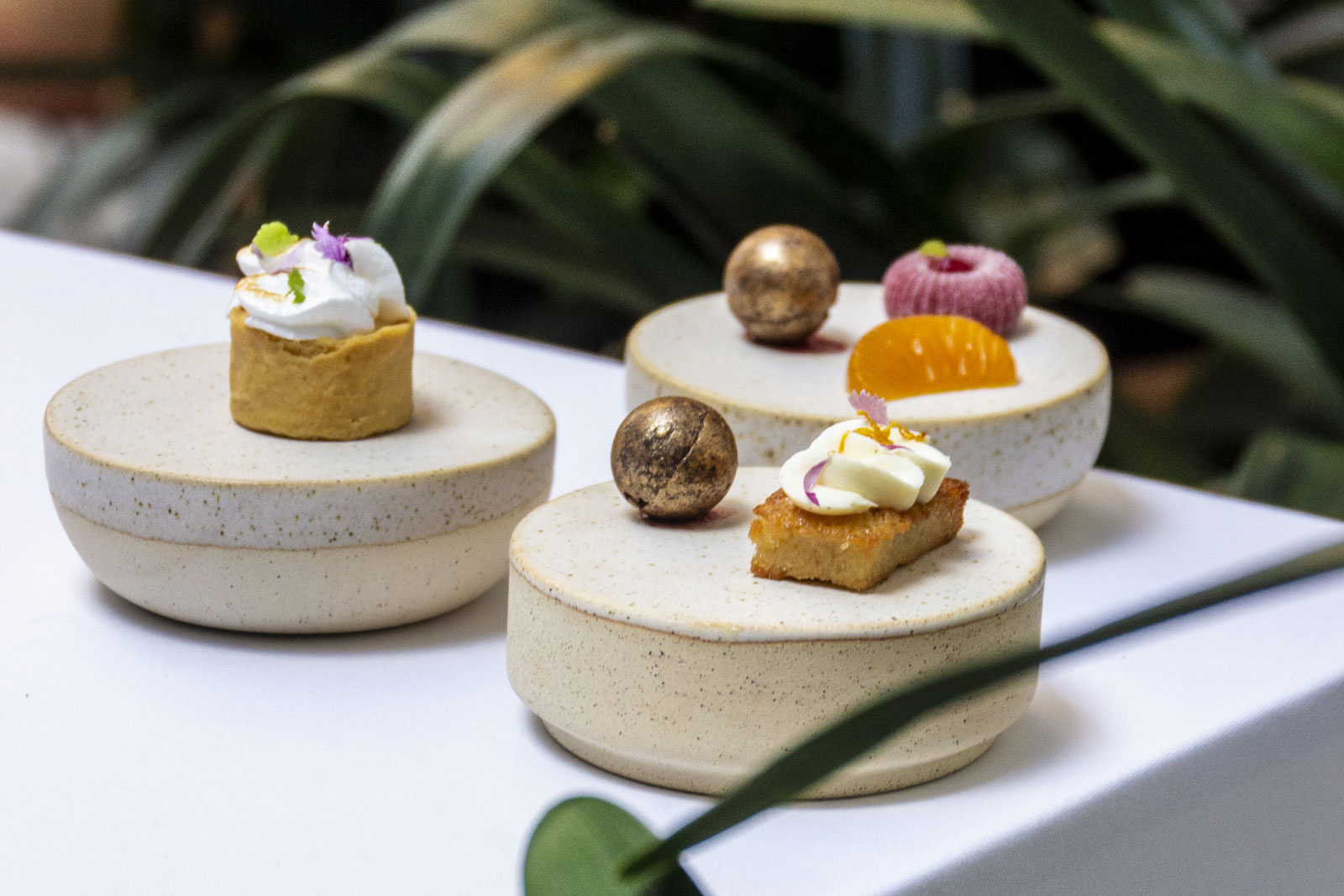 Petitfours van Aromata op drie ronde aardewerken sokkels, met een taartje, een vergulde bol en een partje mandarijn