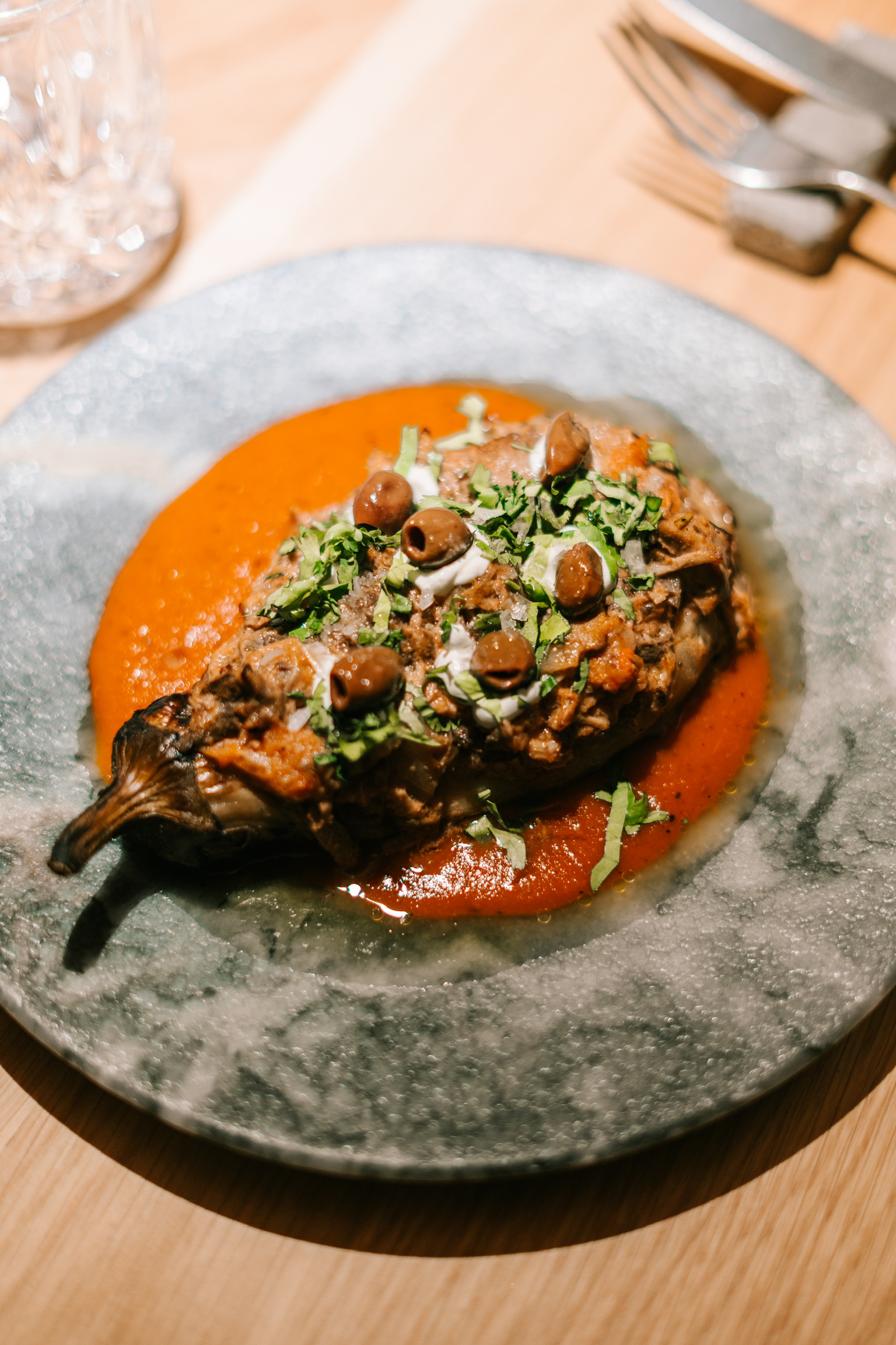 Hele aubergine van de houtskoolgrill bij BàrBar in Palma, op een gemarmerd bord met tomatensaus, olijven en gehakte kruiden