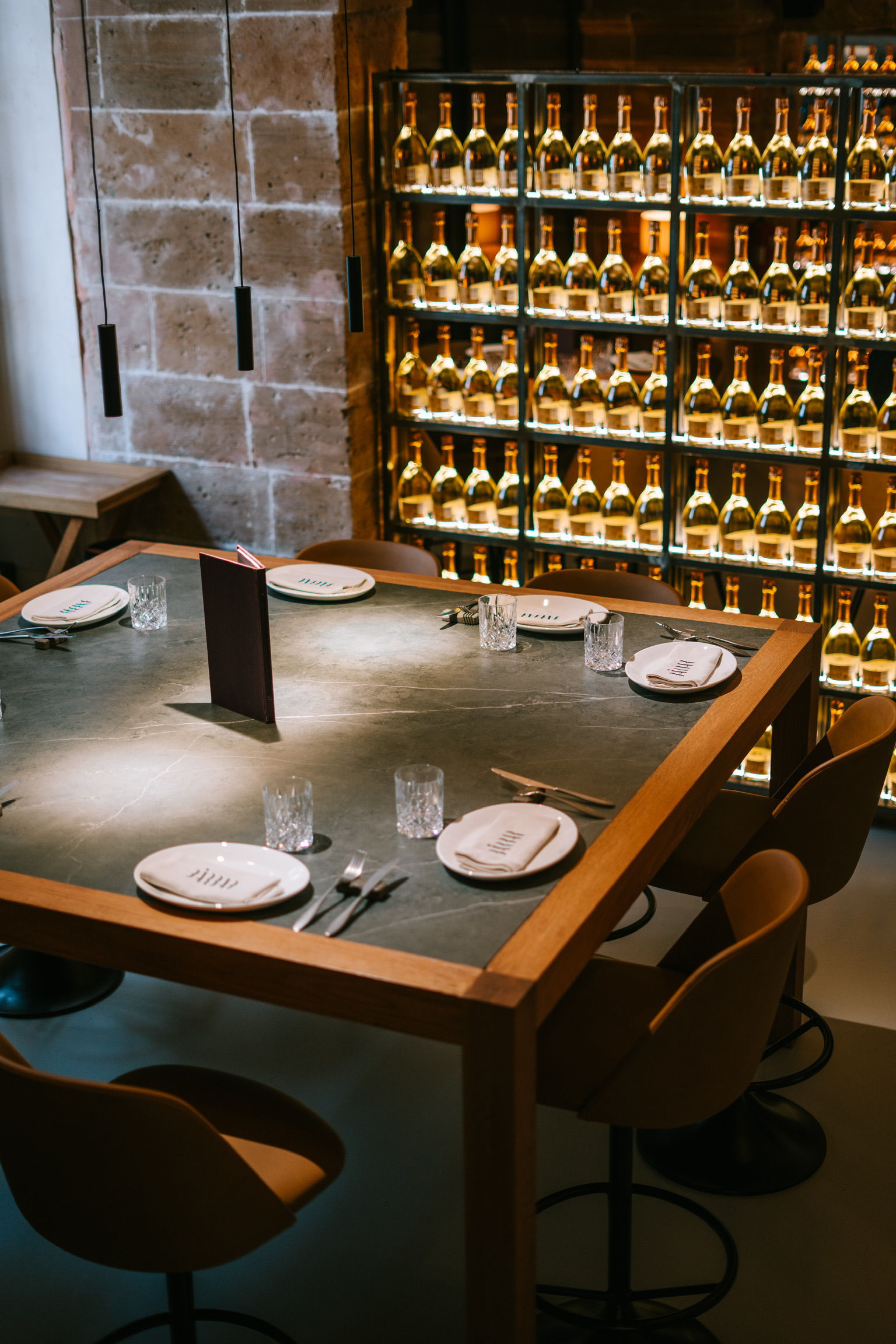 Gedekte tafel met leistenen blad bij BàrBar in Palma, tegen een blootgelegde zandstenen muur en een wand van verlichte wijnflessen
