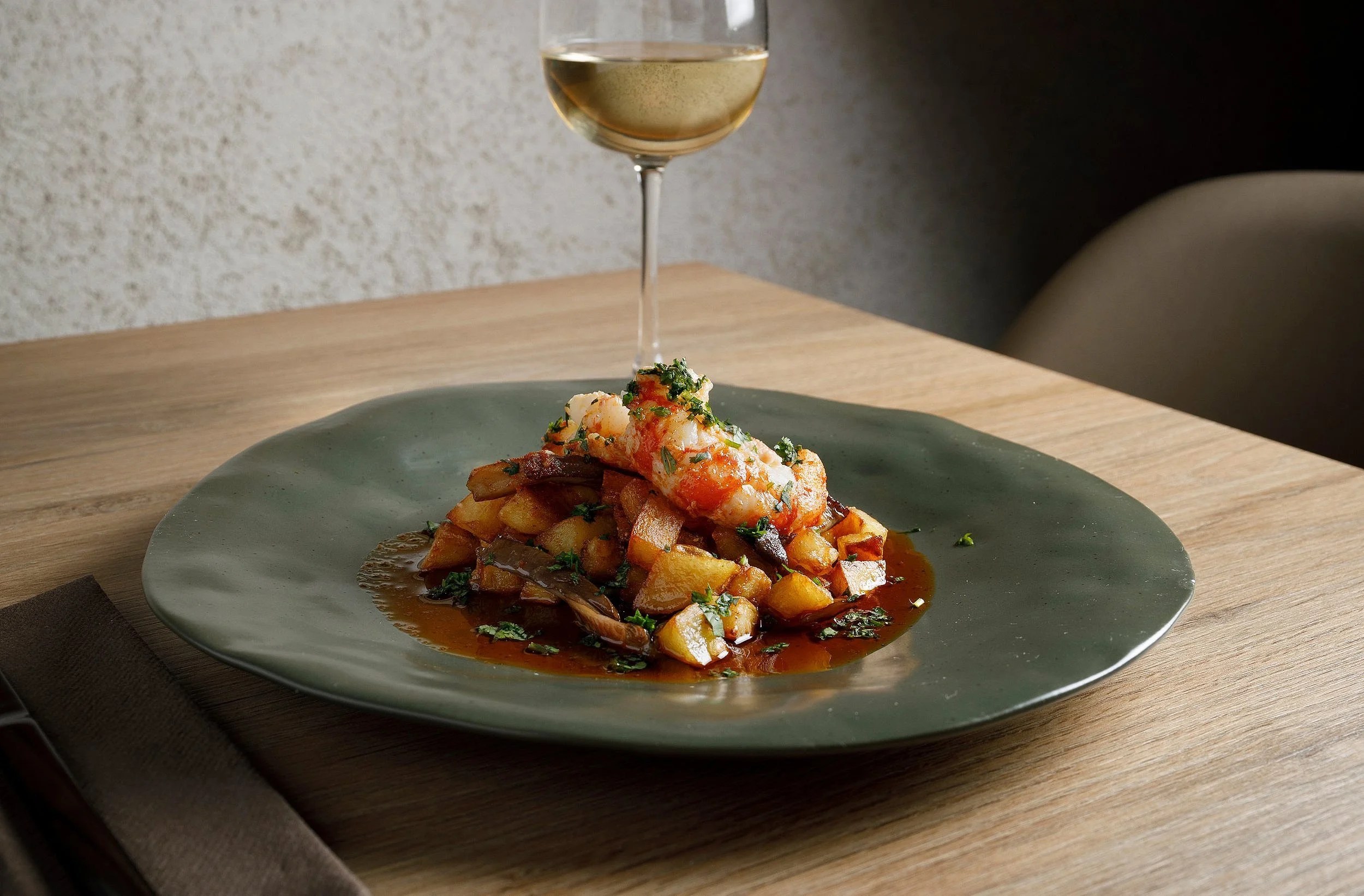Bondo Cocina in Palma: Argentijnse keuken in een oude garage 4 Gerecht op een groen bord met een glas witte wijn op een houten tafel in restaurant Bondo Cocina