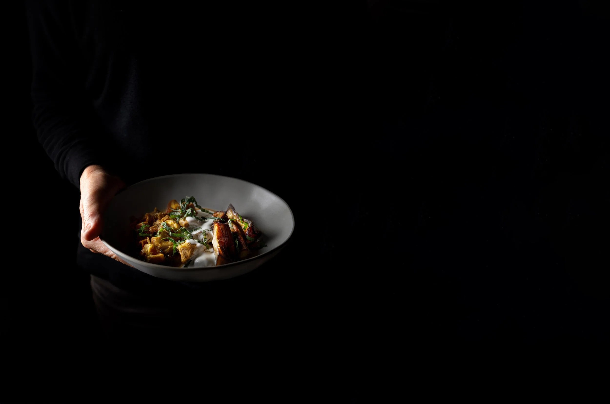 Bondo Cocina in Palma: Argentijnse keuken in een oude garage 6 Een hand houdt een donkere kom met een gerecht van Bondo Cocina tegen een zwarte achtergrond
