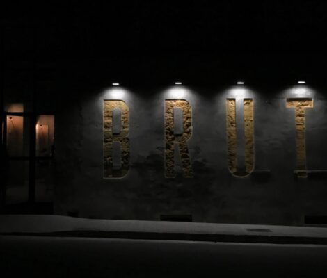 De verlichte gevel van restaurant Brut in Llubí op Mallorca, met de naam in grote letters uitgehakt in de muur