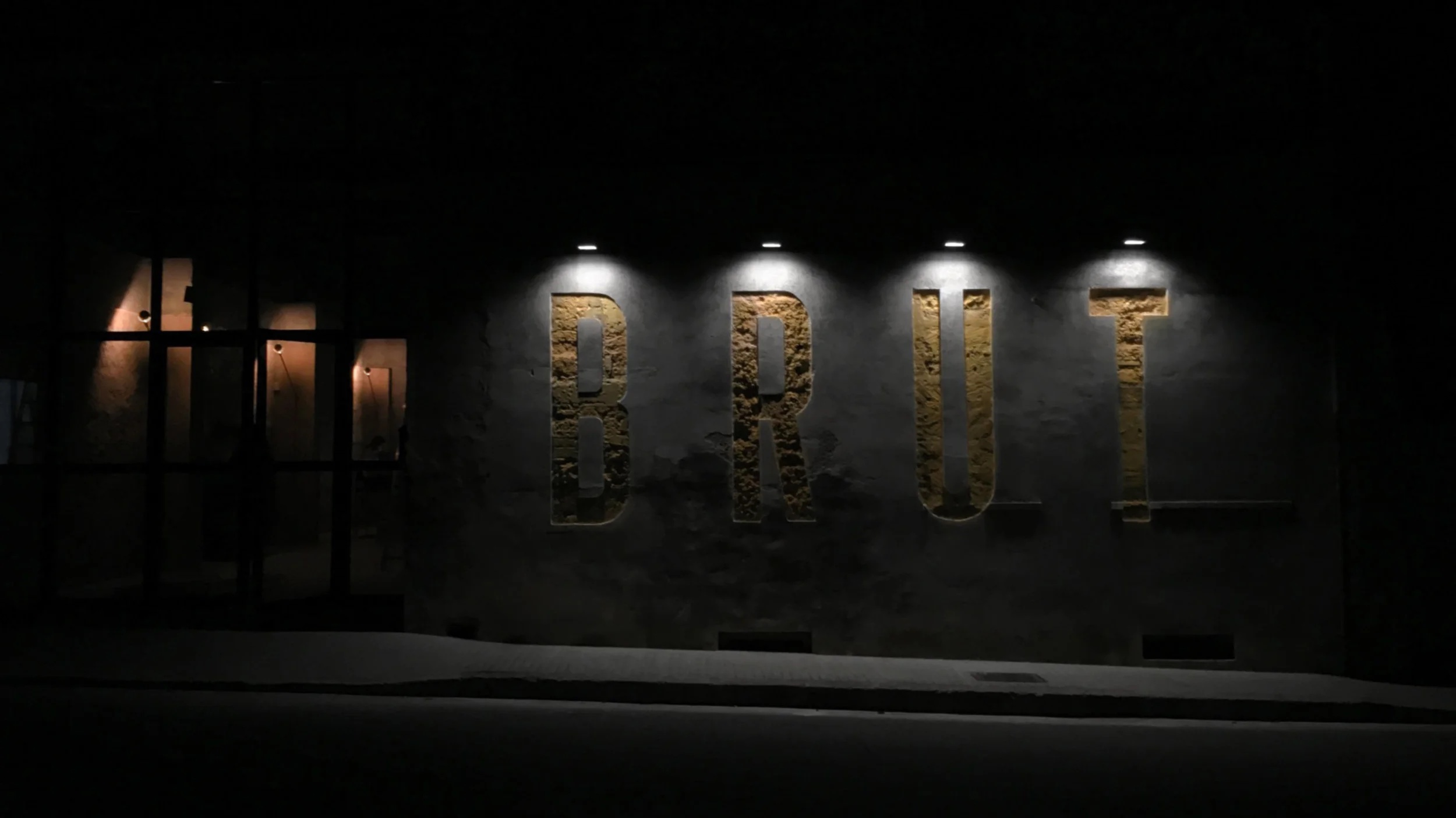 Brut in Llubí: één zitting per avond in een oude houtloods 1 De verlichte gevel van restaurant Brut in Llubí op Mallorca, met de naam in grote letters uitgehakt in de muur