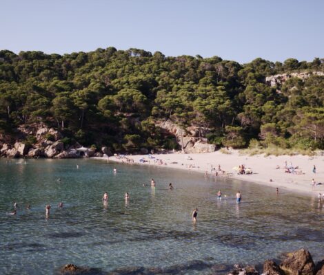 De baai van Cala Algaiarens op Menorca met wit zandstrand, turquoise water en dennenbos op de hellingen