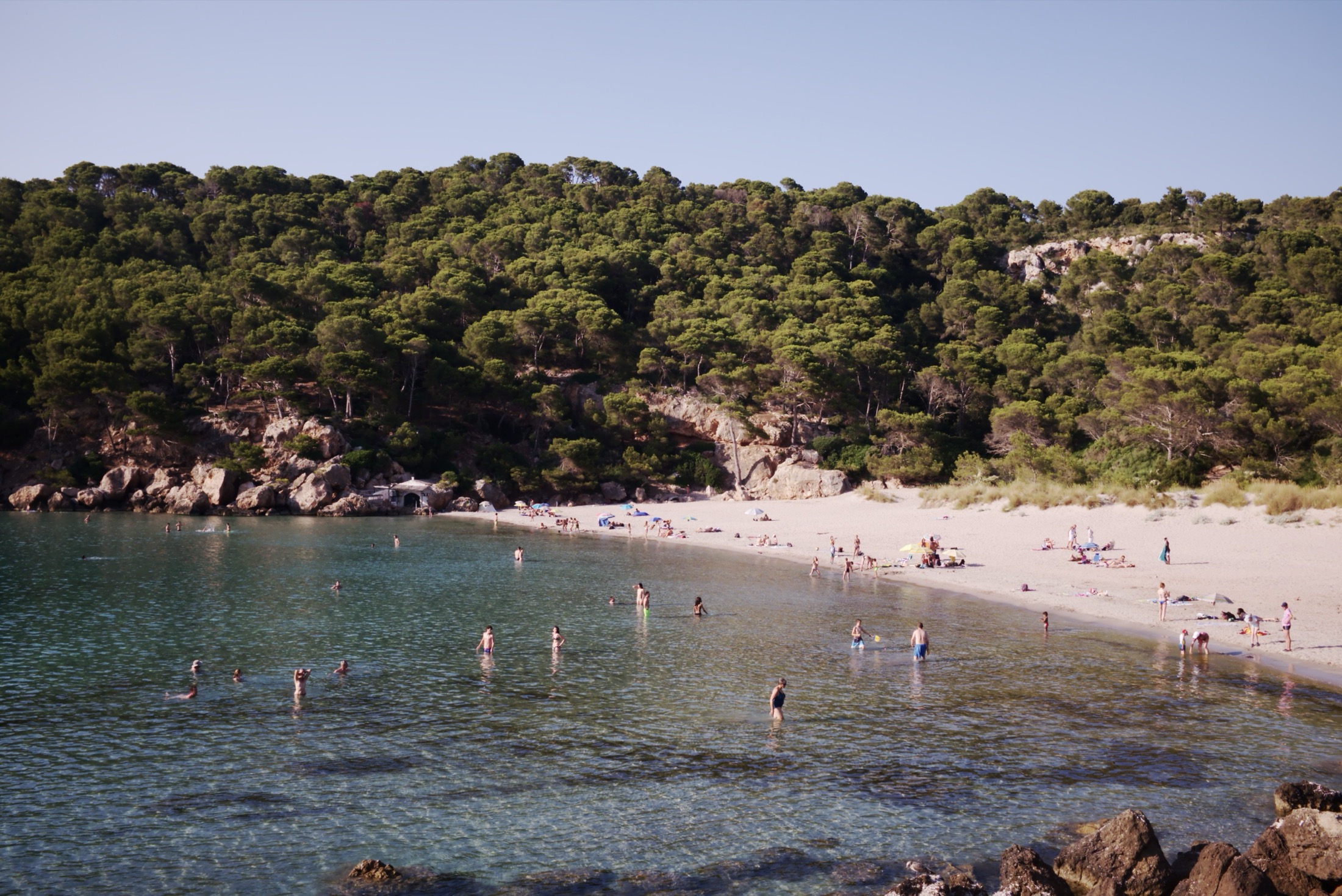 De baai van Cala Algaiarens op Menorca met wit zandstrand, turquoise water en dennenbos op de hellingen
