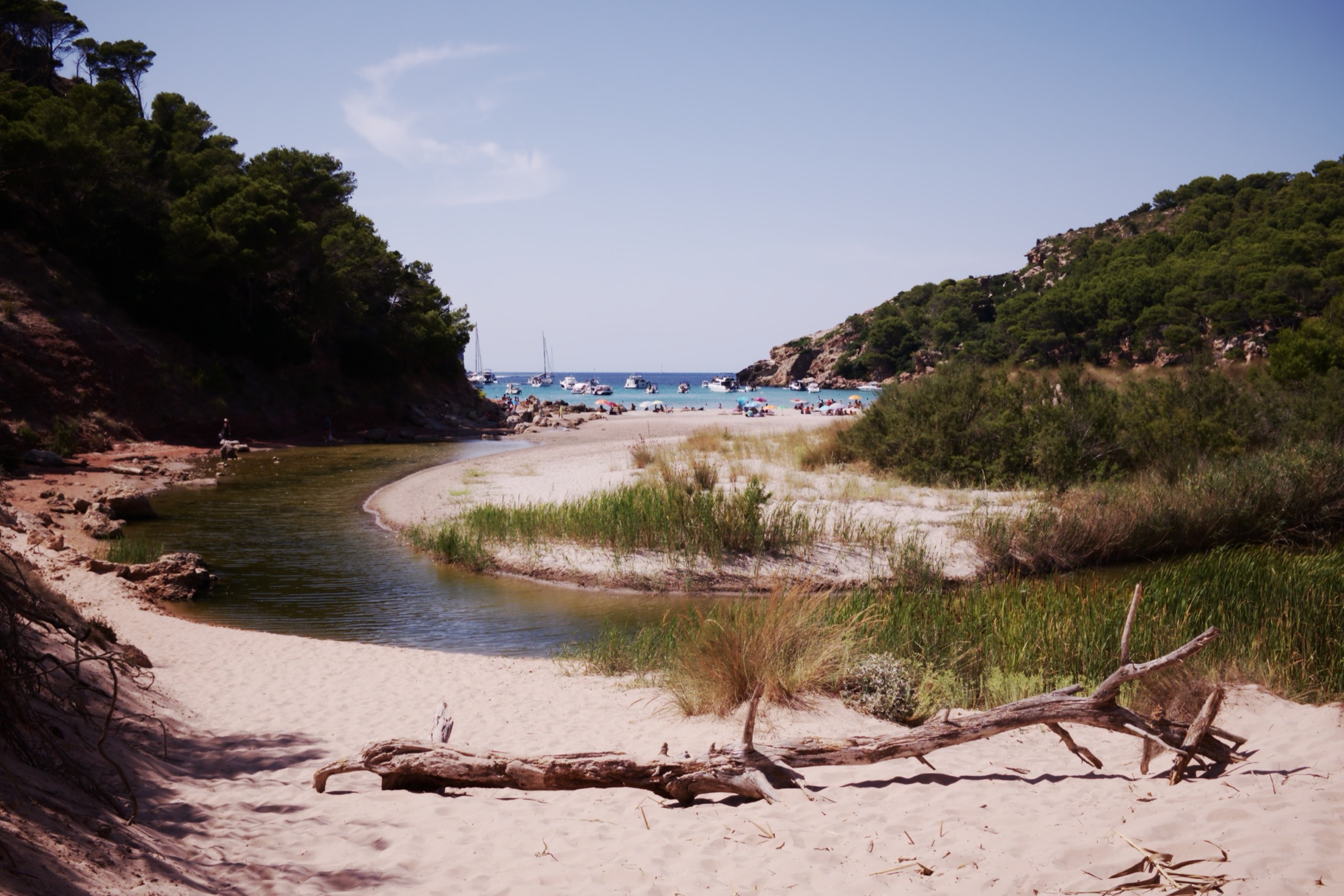 De Torrent de la Vall kronkelt door het zand naar het strand van Cala Algaiarens, met boten in de baai