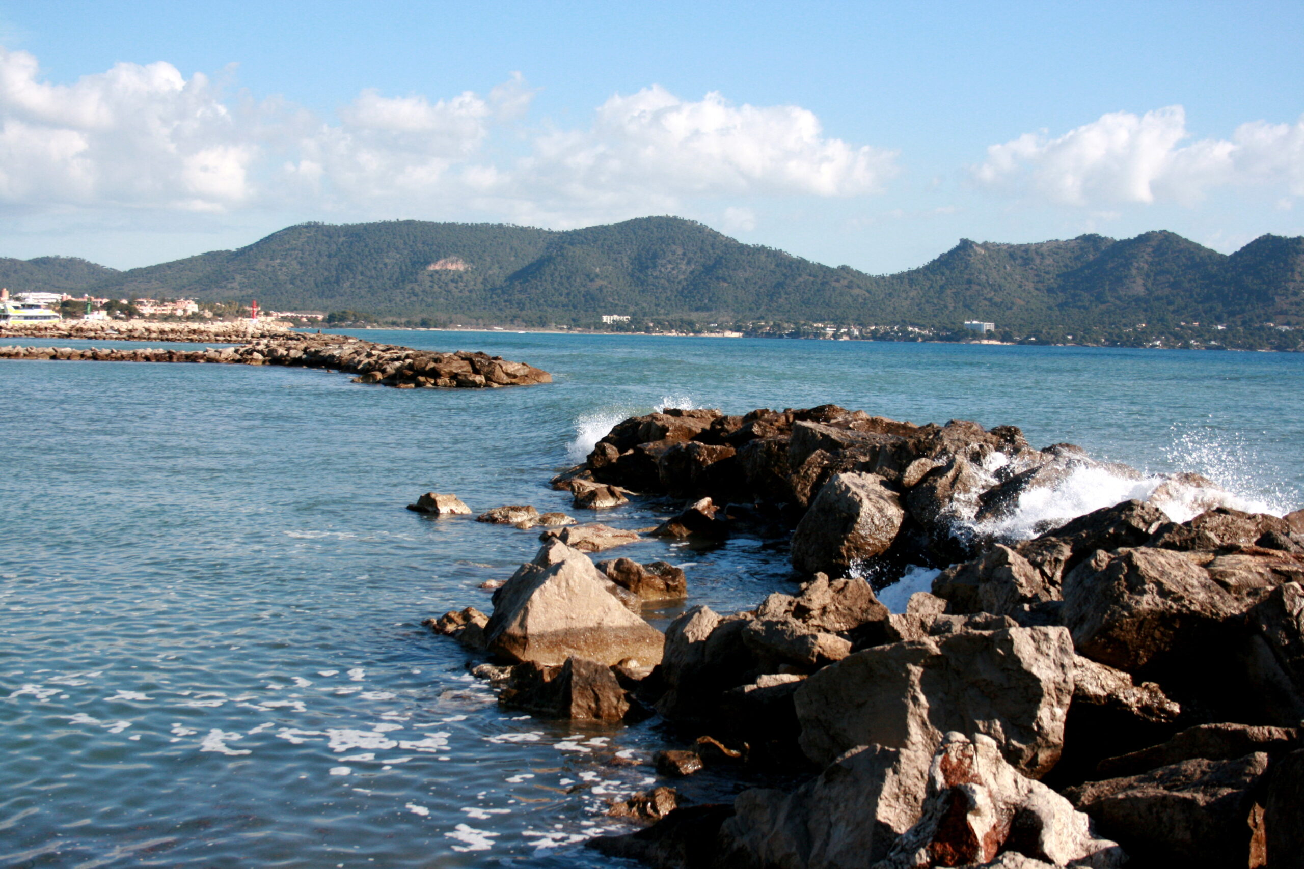 Branding die stukslaat op de rotsblokken aan de kust van Cala Bona, met de baai en de heuvels achter Cala Millor op de achtergrond