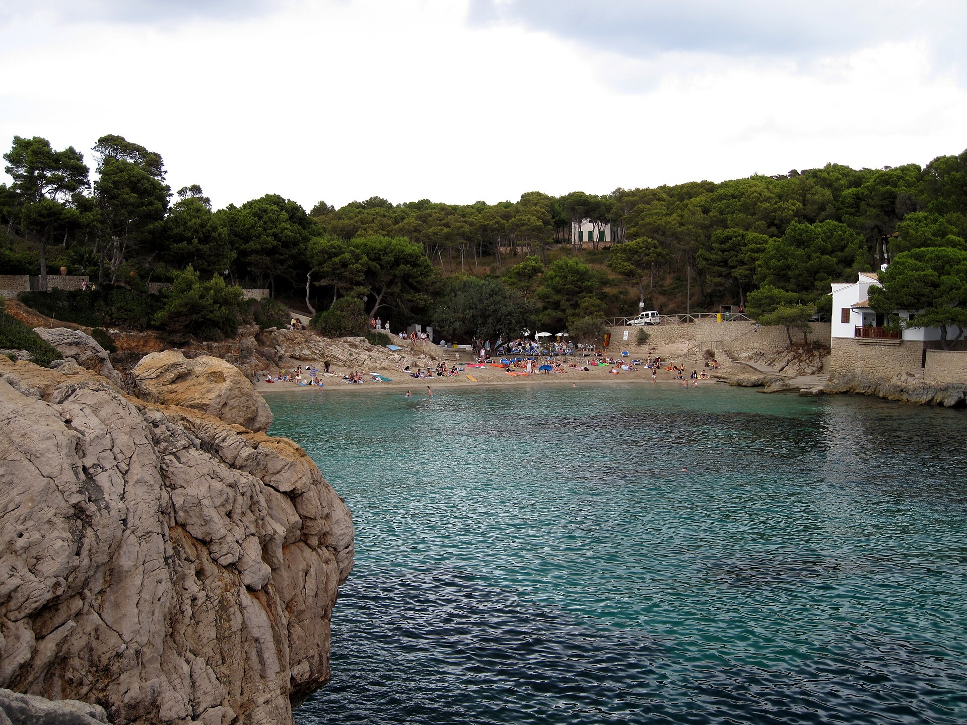 Cala Gat gezien vanaf de rotsen aan de westkant, met het strandje, de kiosk en het beboste heuvelland erachter