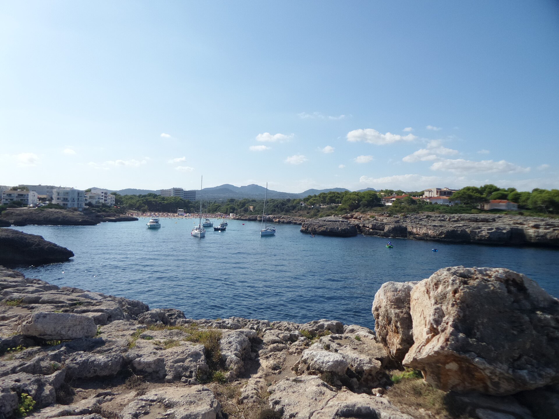 De baai van Cala Marçal gezien vanaf de rotsrichel, met ankerende bootjes op het water en de bebouwing aan de overkant