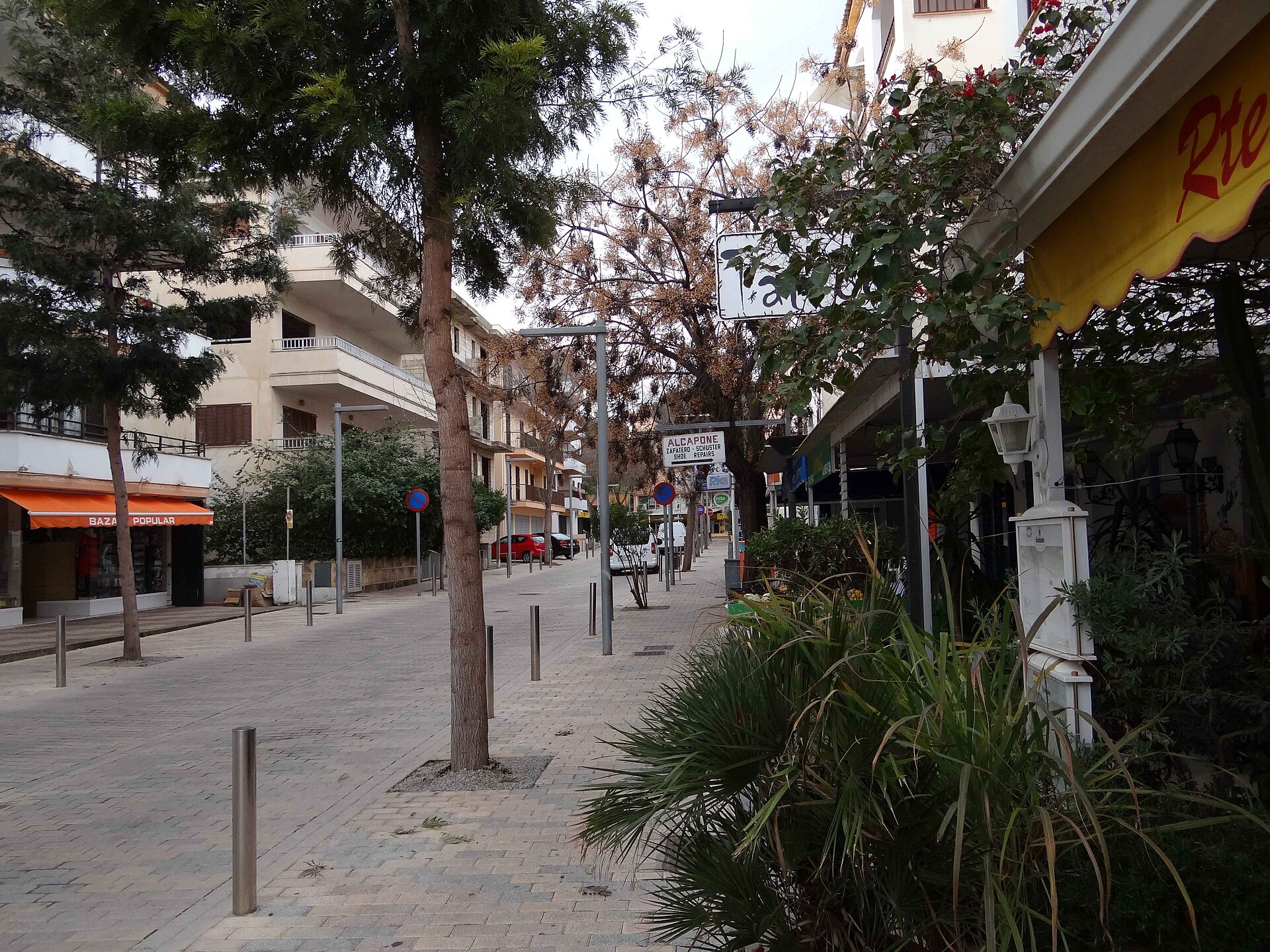 Een autovrije winkelstraat in het centrum van Cala Millor met bomen, terrassen en winkelpuien