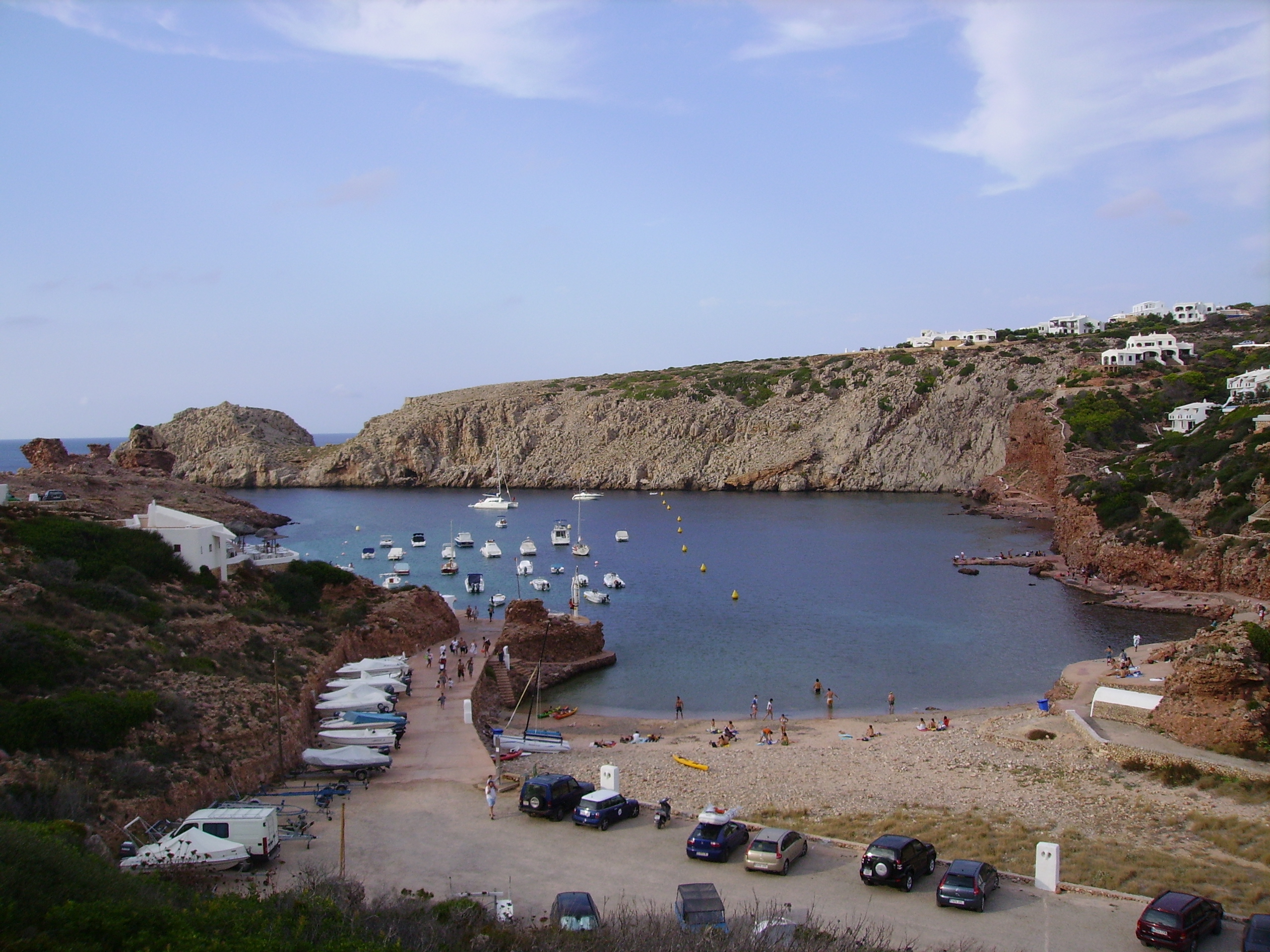 Cala Morell Menorca: witte huizen, grafgrotten en een klein rotsstrand 4 Overzicht van de smalle baai van Cala Morell met het kiezelstrand, de helling met bootjes en de witte huizen