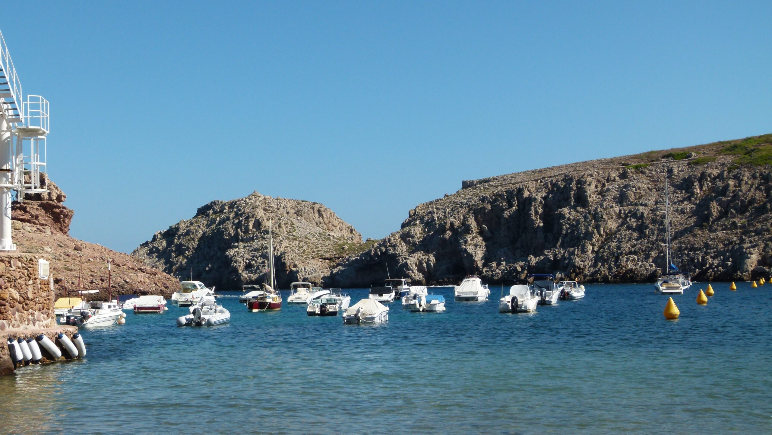 Cala Morell Menorca: witte huizen, grafgrotten en een klein rotsstrand 5 Bootjes aan boeien in de beschutte baai van Cala Morell met de kliffen op de achtergrond