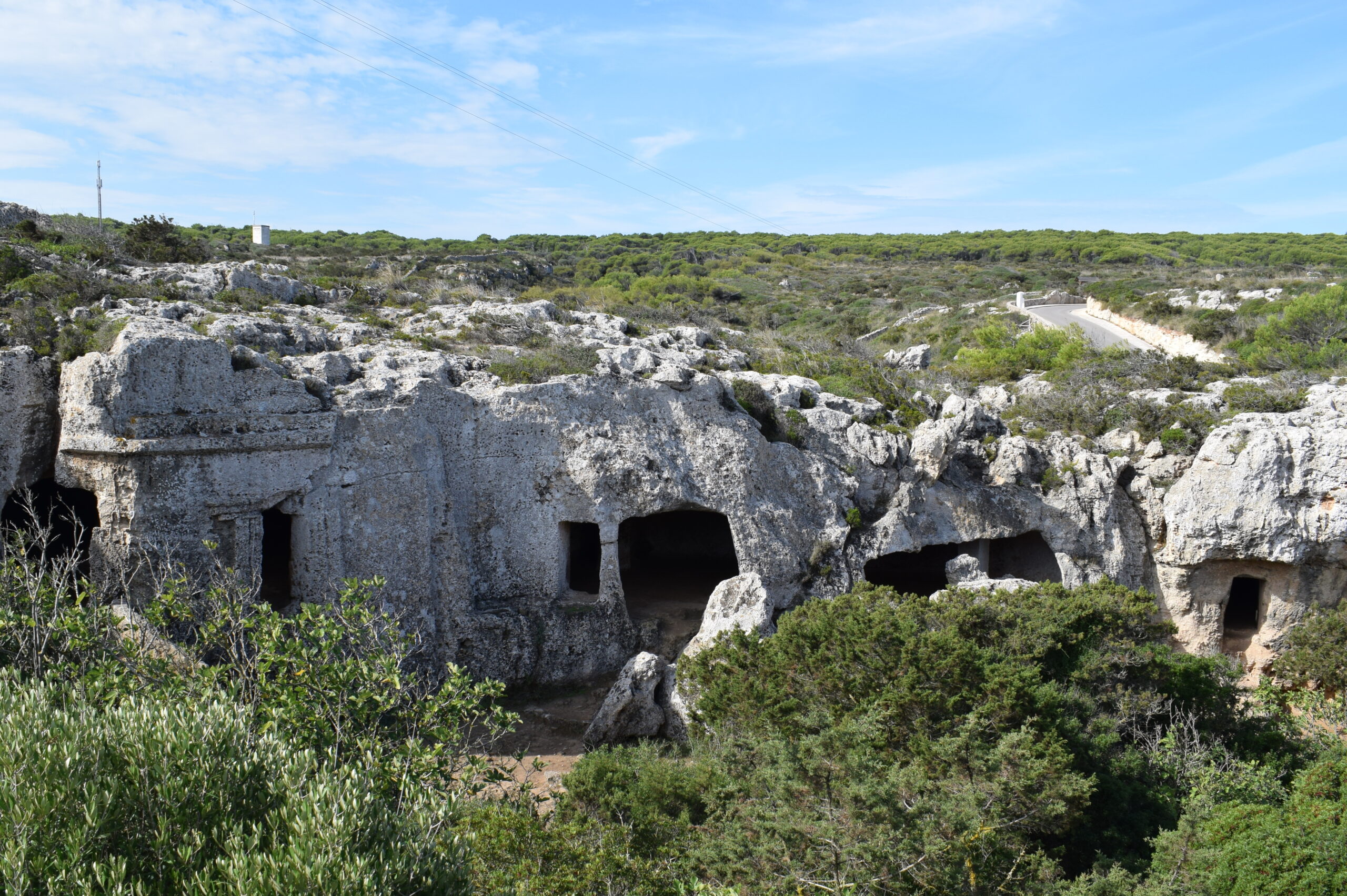 Cala Morell Menorca: witte huizen, grafgrotten en een klein rotsstrand 2 Rij uitgehouwen grafgrotten in de kalkstenen ravijnwand van de necropolis van Cala Morell