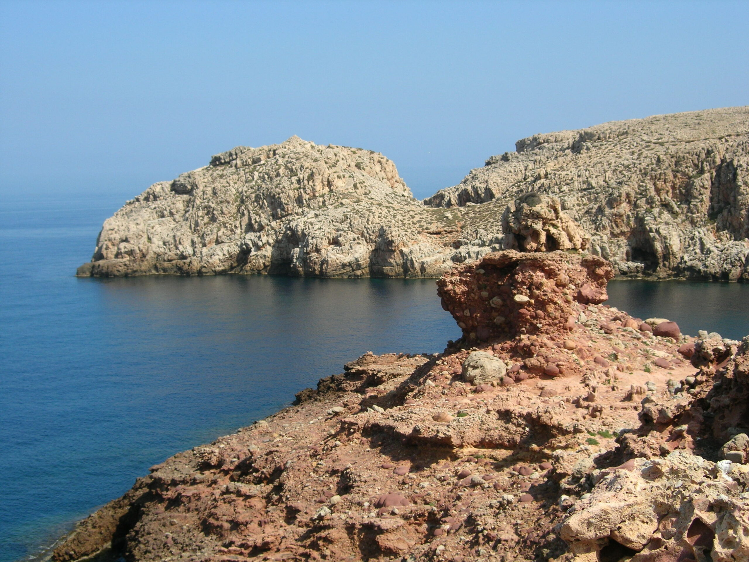 Cala Morell Menorca: witte huizen, grafgrotten en een klein rotsstrand 7 Het rode conglomeraat op de voorgrond en de grijze dolomietkaap aan de overkant van Cala Morell