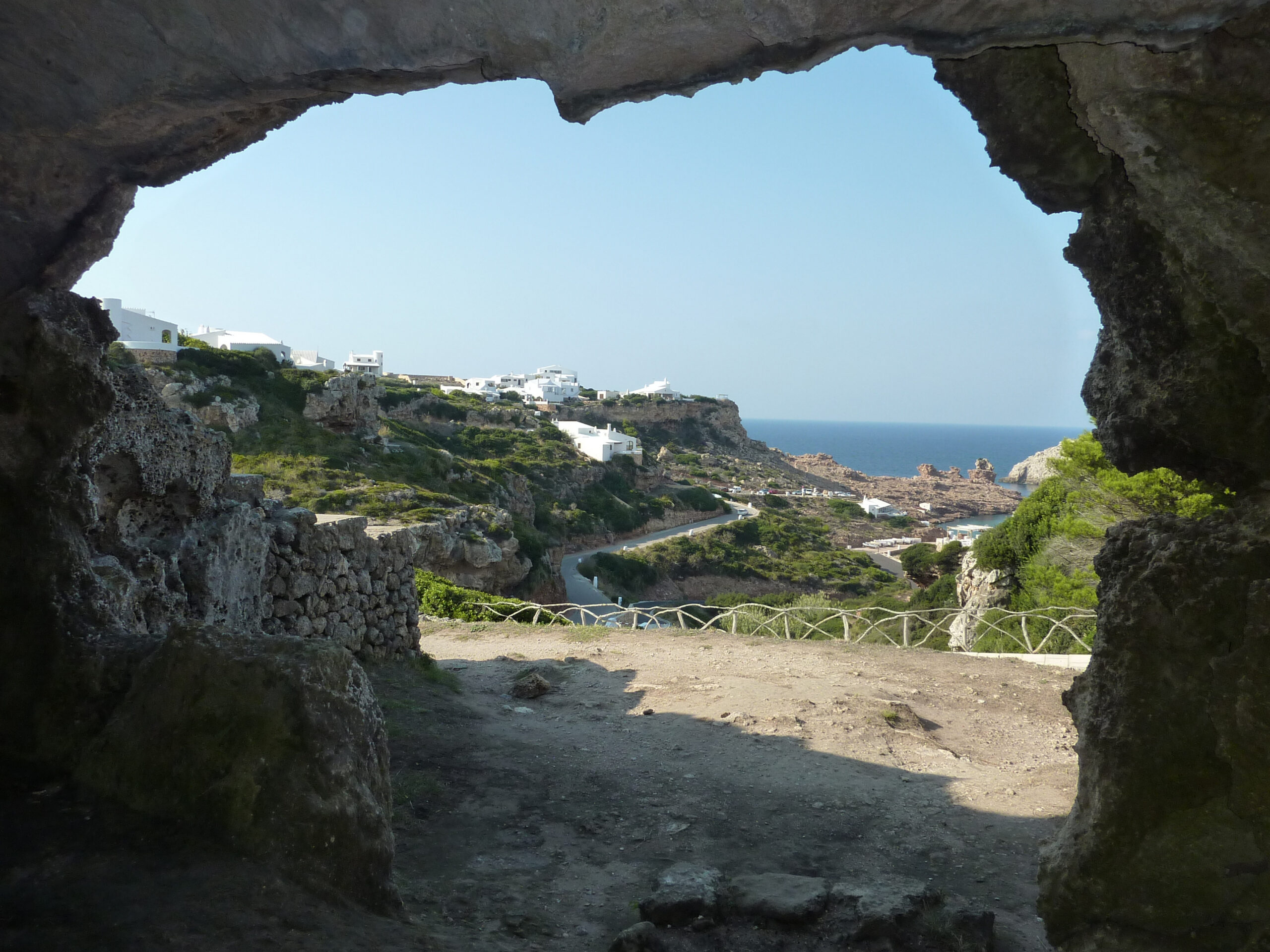 Cala Morell Menorca: witte huizen, grafgrotten en een klein rotsstrand 10 Uitzicht vanuit een van de grafgrotten over het ravijn naar de witte huizen en de zee bij Cala Morell