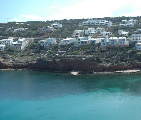 Witte kubusvormige huizen in terrassen boven het turquoise water van Cala Morell op Menorca