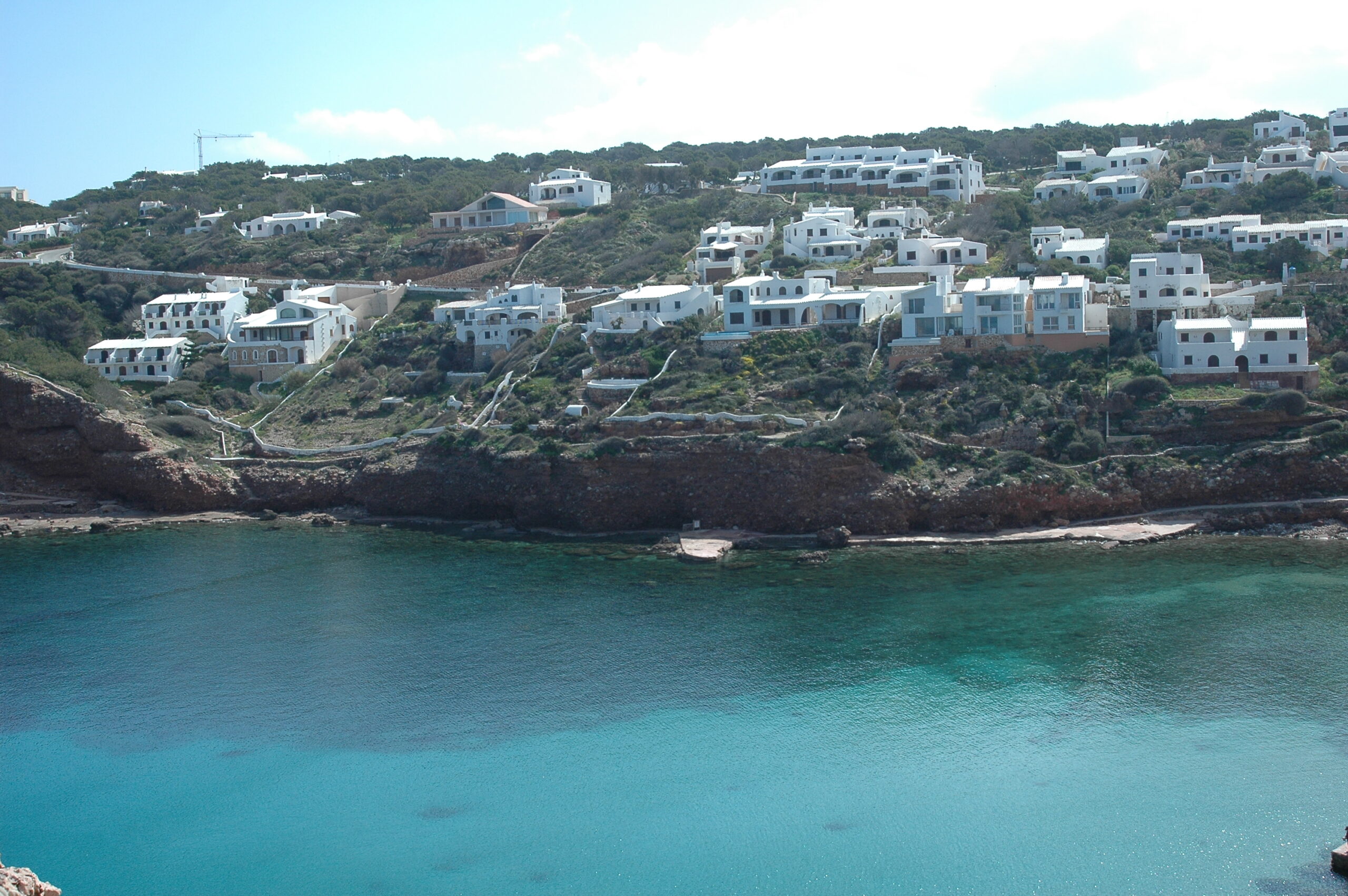 Cala Morell Menorca: witte huizen, grafgrotten en een klein rotsstrand 1 Witte kubusvormige huizen in terrassen boven het turquoise water van Cala Morell op Menorca