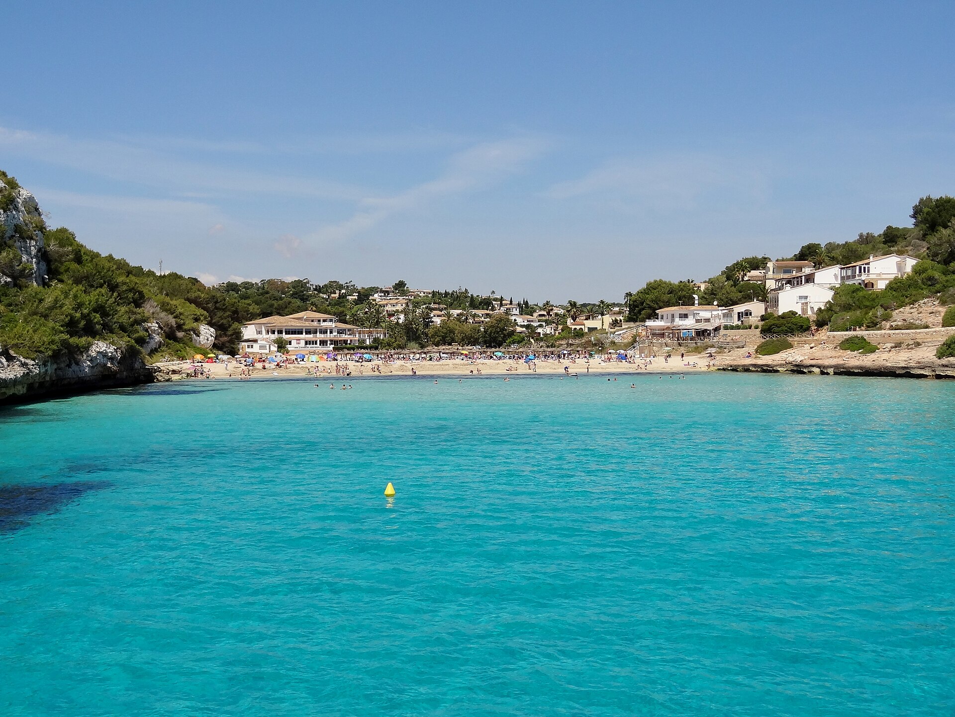 De monding van Cala Romàntica met de rotsrichel aan de zijkant en het diepere donkerblauwe water buiten de baai