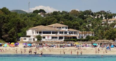 Cala Romàntica Mallorca: het strand dat eigenlijk s'Estany d'en Mas heet 8 Het strand van Cala Romàntica in het hoogseizoen, met een lange rij rieten parasols, badgasten op het lichte zand, turquoise water en het hotel en de pijnbomen erachter