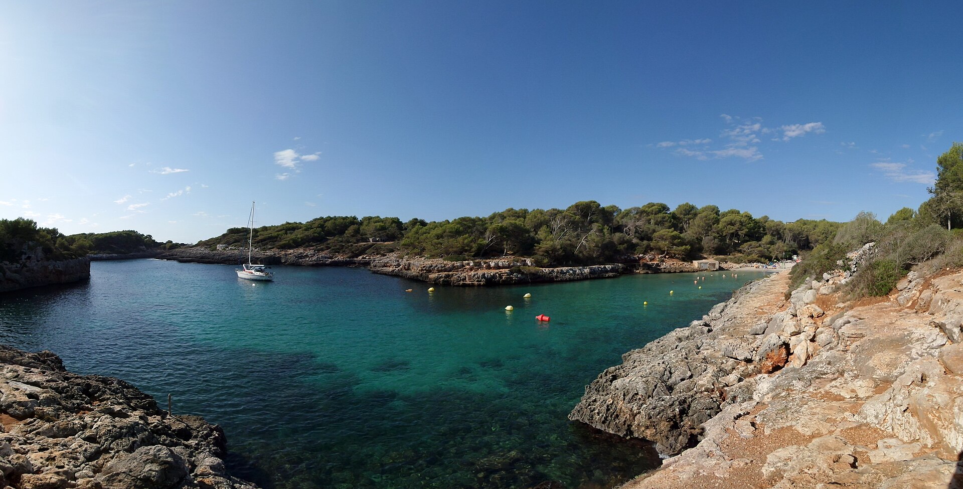 Cala sa Nau Mallorca: de smalle pijnboombaai bij Felanitx 4 Panorama van de inham van Cala sa Nau met een zeilboot voor anker, de boeienlijn van het zwemgebied en het strand aan het eind