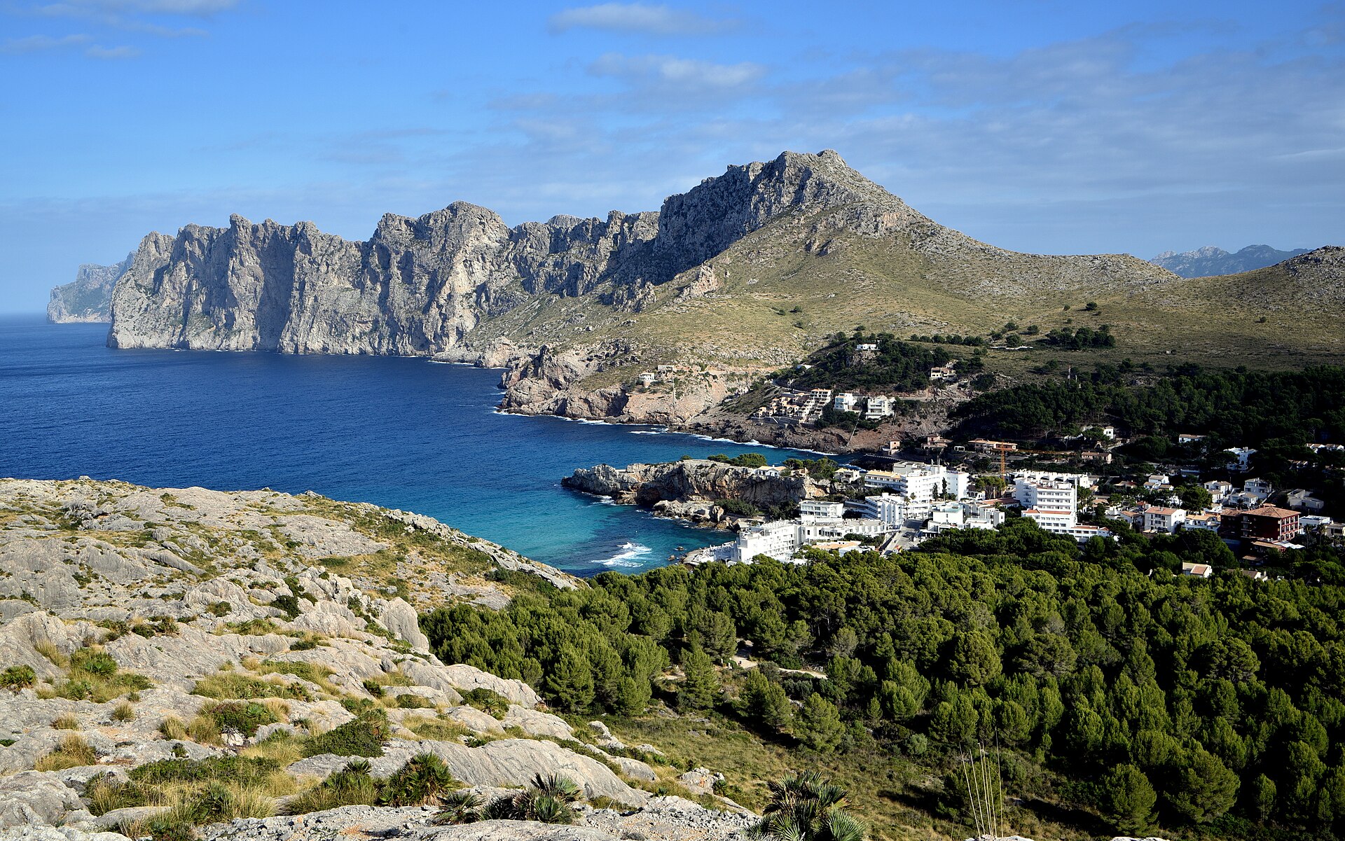 Overzicht van de baai van Cala Sant Vicenç met de witte huizen tussen de pijnbossen en de gekartelde bergkam die de baai afsluit