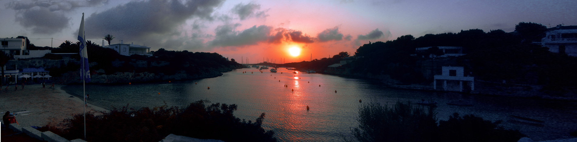 Cala Santandría Menorca: de beschutte kreek bij Ciutadella en de Torre des Castellar 3 Panorama van Cala Santandría bij zonsondergang, met de zon die recht in de opening van de smalle kreek zakt