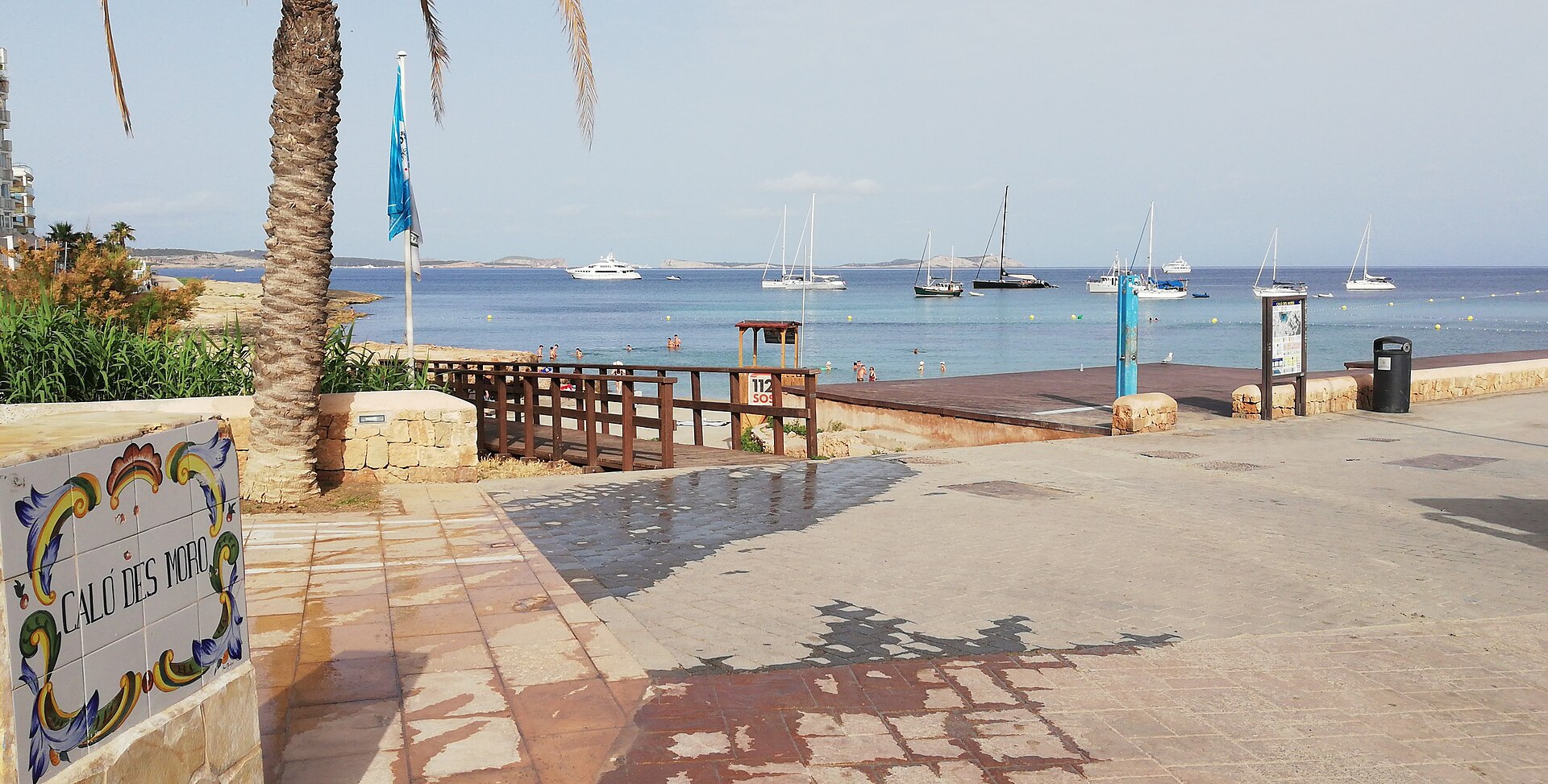 Caló des Moro Ibiza: het strandje aan de Sunset Strip van Sant Antoni 2 Het keramische naambord Caló des Moro aan de promenade van Sant Antoni, met de baai, de ankerende zeilboten en de eilandjes erachter