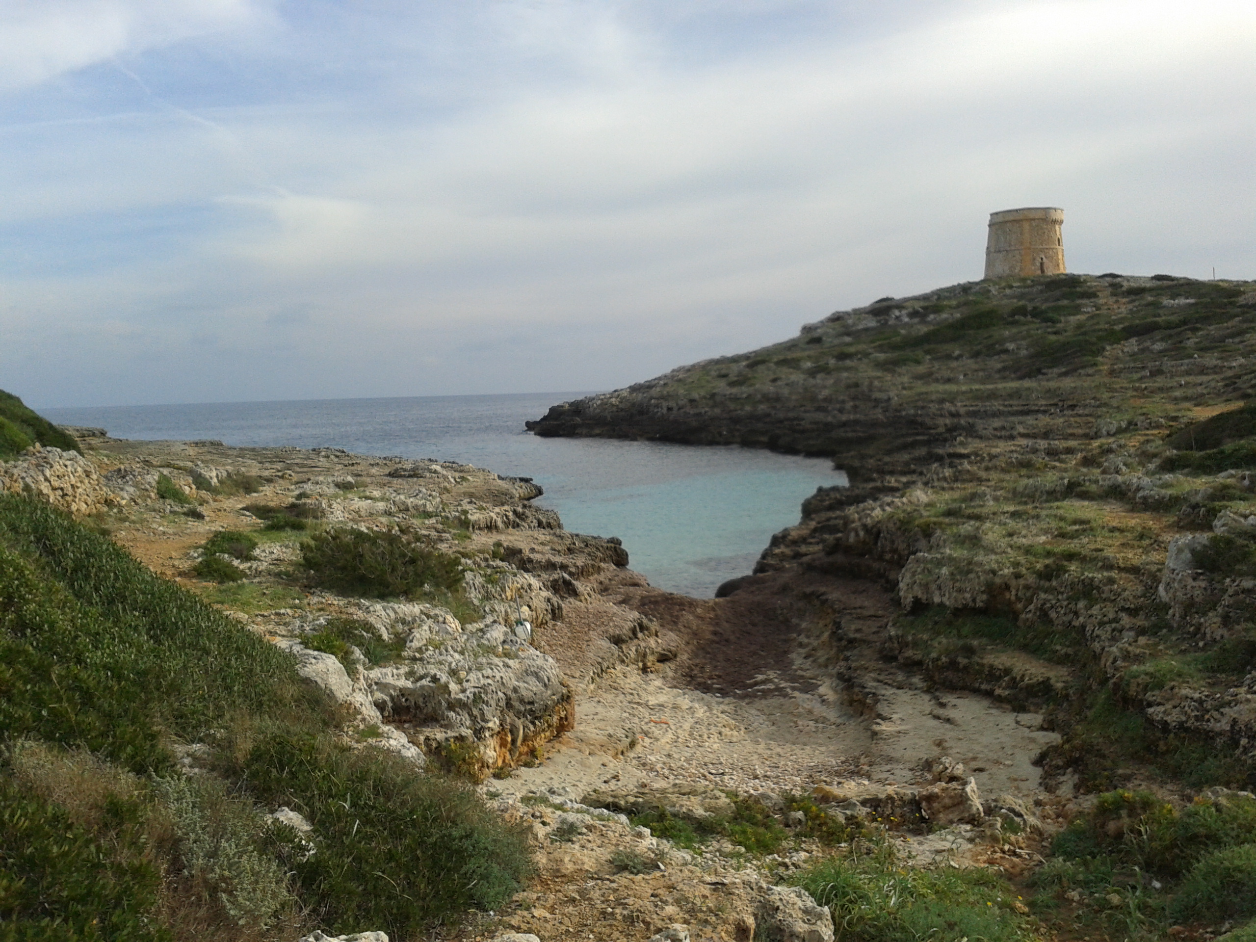 Het smalle rotsinhammetje Caló Roig bij Sant Lluís op Menorca met een wachttoren op de kop erachter