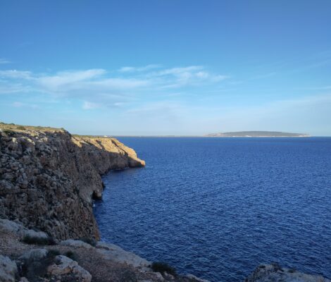 De kale kliffen van Cap de Barbaria op Formentera boven diepblauwe zee, met La Mola in de verte
