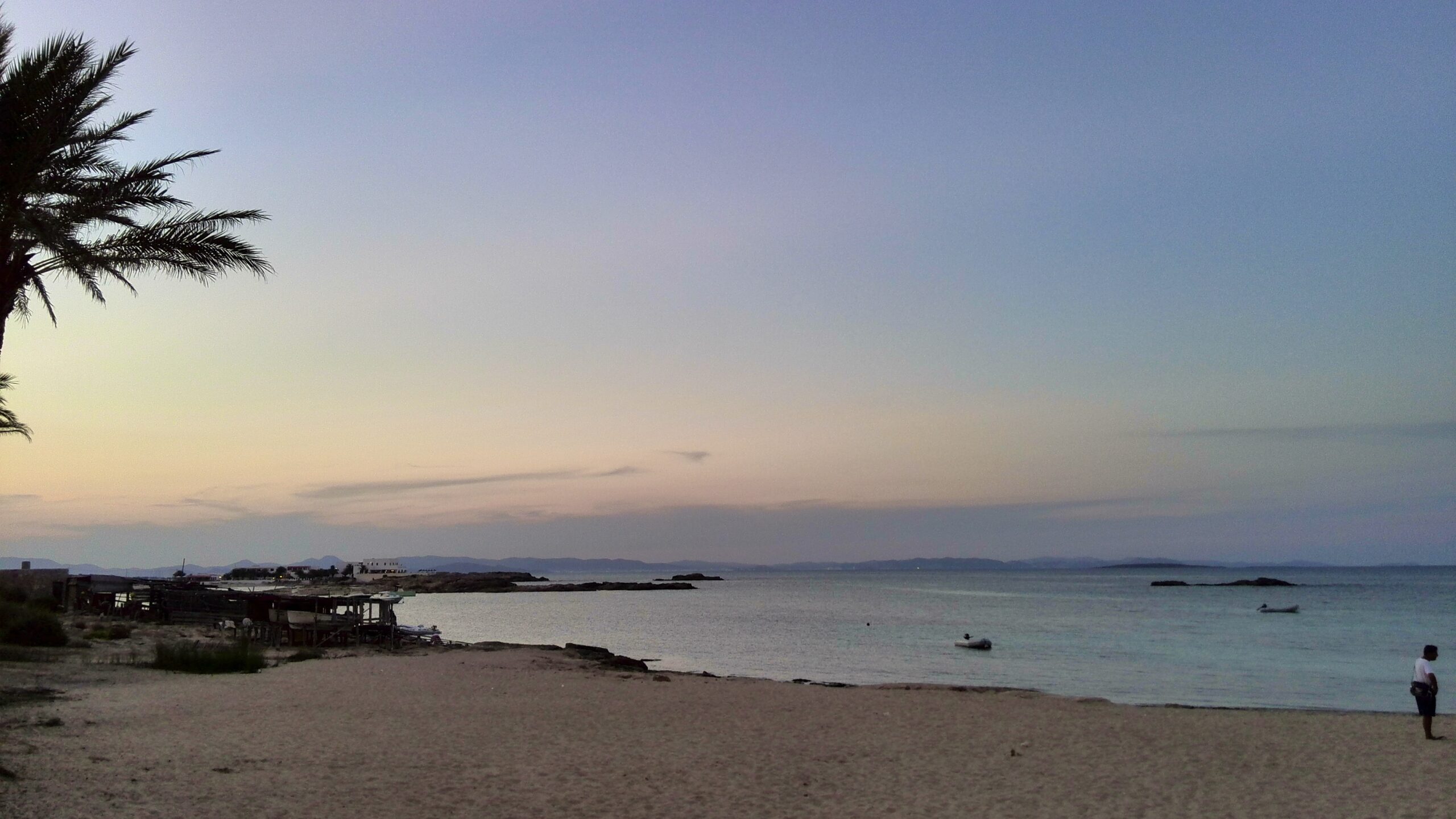 Het strand van Es Pujols op Formentera bij schemer, met palmen en de oude botenhuizen aan de rand