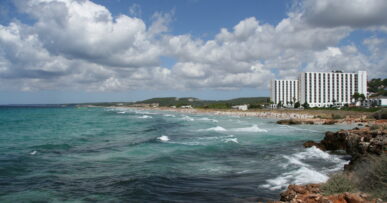 Kamperen op Menorca: twee campings, en waarom de rest niet mag 3 Het lange strand van Son Bou op Menorca met zand, branding en de beboste heuvels erachter