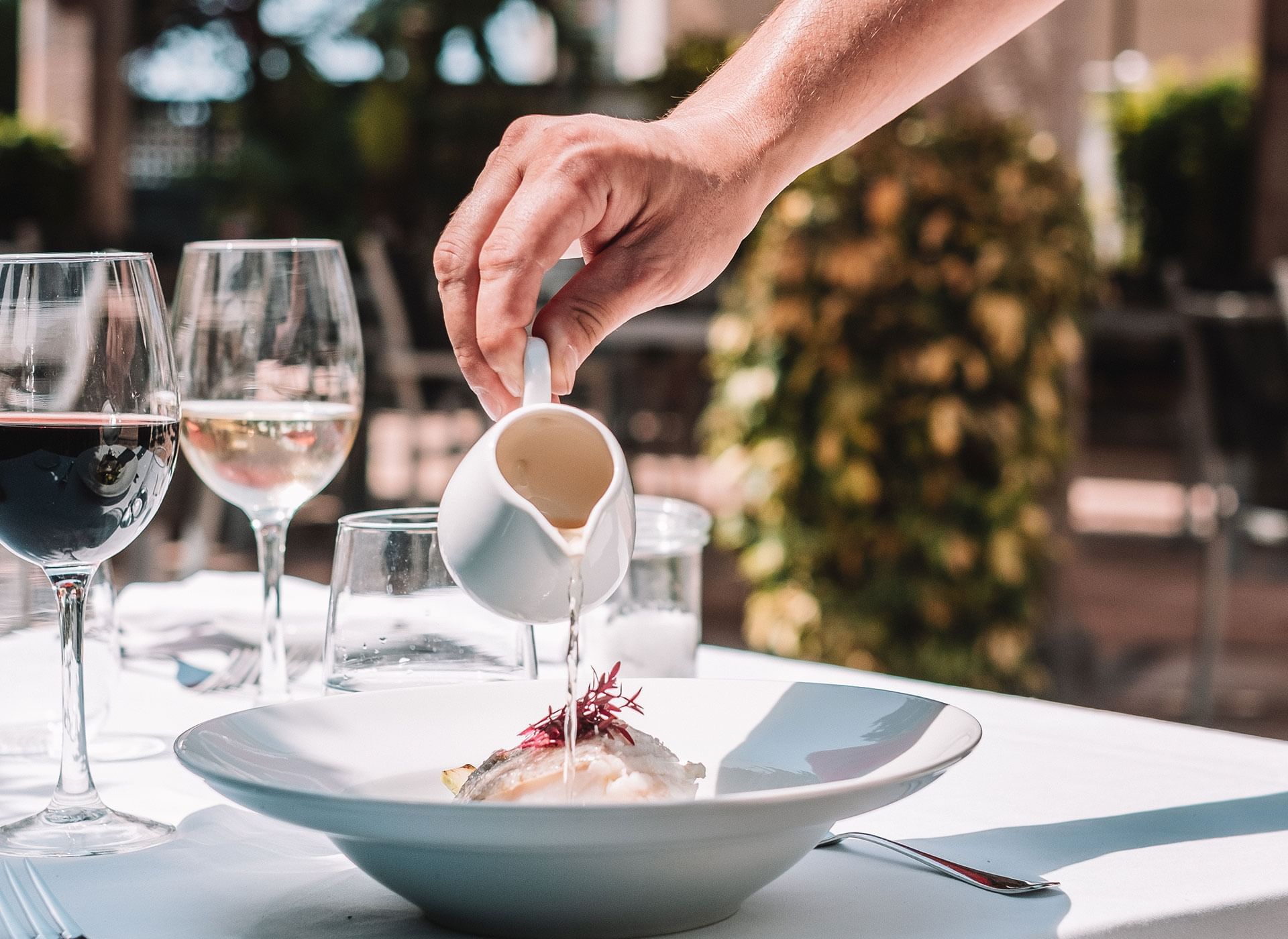 Ca'n Blau Sóller: het restaurant van het Gran Hotel uit 1880 6 Een hand schenkt saus uit een kannetje over een bord aan een gedekte tafel in het Gran Hotel Sóller