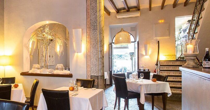 Ca'n Boqueta (Sóller): Bib Gourmand aan de Gran Via 1 De eetzaal van restaurant Ca'n Boqueta in Sóller met witte tafellakens, houten balkenplafond, een stenen vloer en een trap met beschilderde tegels