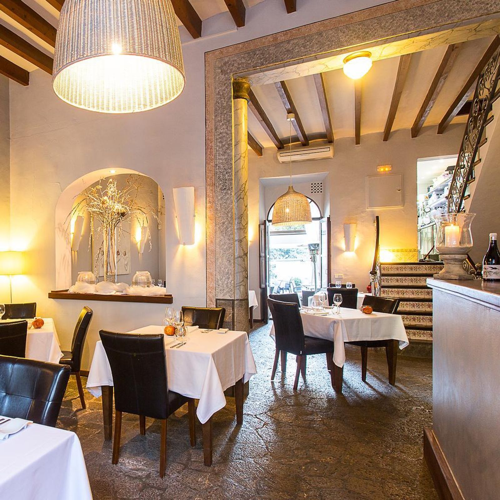 Ca'n Boqueta (Sóller): Bib Gourmand aan de Gran Via 1 De eetzaal van restaurant Ca'n Boqueta in Sóller met witte tafellakens, houten balkenplafond, een stenen vloer en een trap met beschilderde tegels