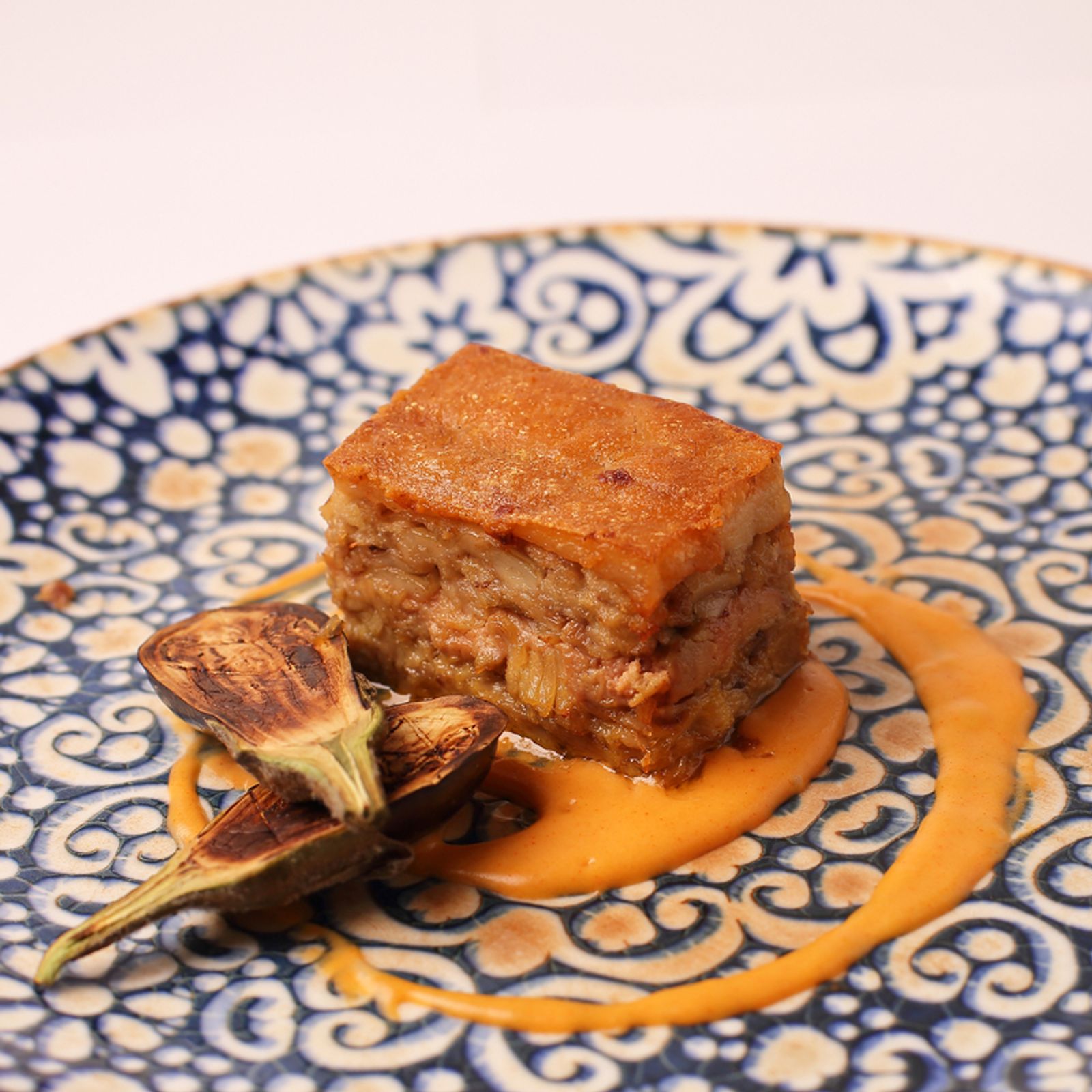 Ca'n Boqueta (Sóller): Bib Gourmand aan de Gran Via 2 Blok gegaarde porcella met krokante korst, een geroosterde artisjok en oranje puree op een blauw bewerkt Mallorcaans bord bij Ca'n Boqueta