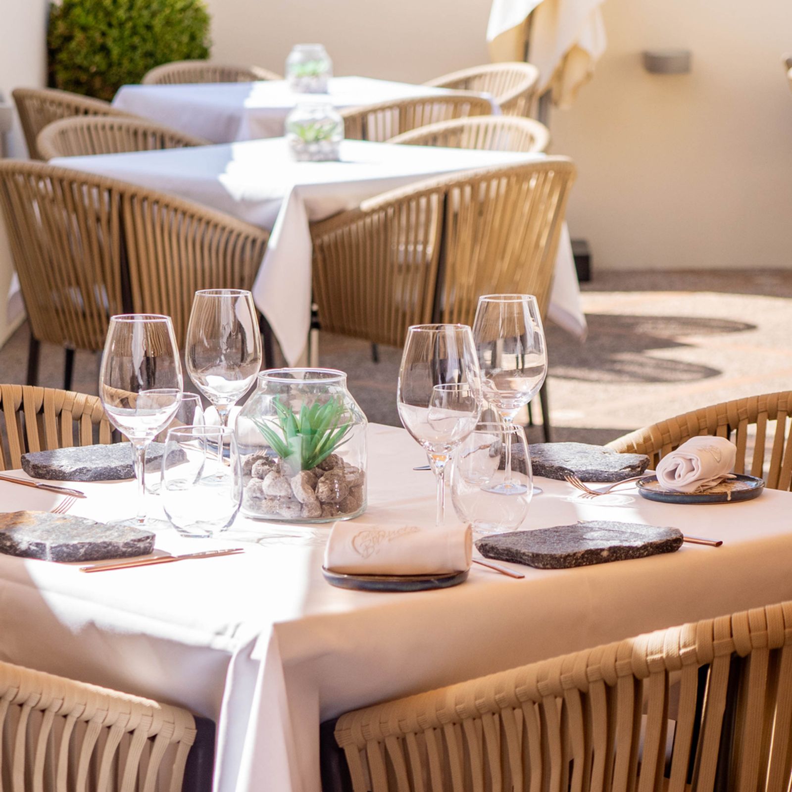 Ca'n Boqueta (Sóller): Bib Gourmand aan de Gran Via 8 Het binnenterras van Ca'n Boqueta in Sóller met wit gedekte tafels, rieten stoelen en stenen plaatjes als onderzetter op het couvert