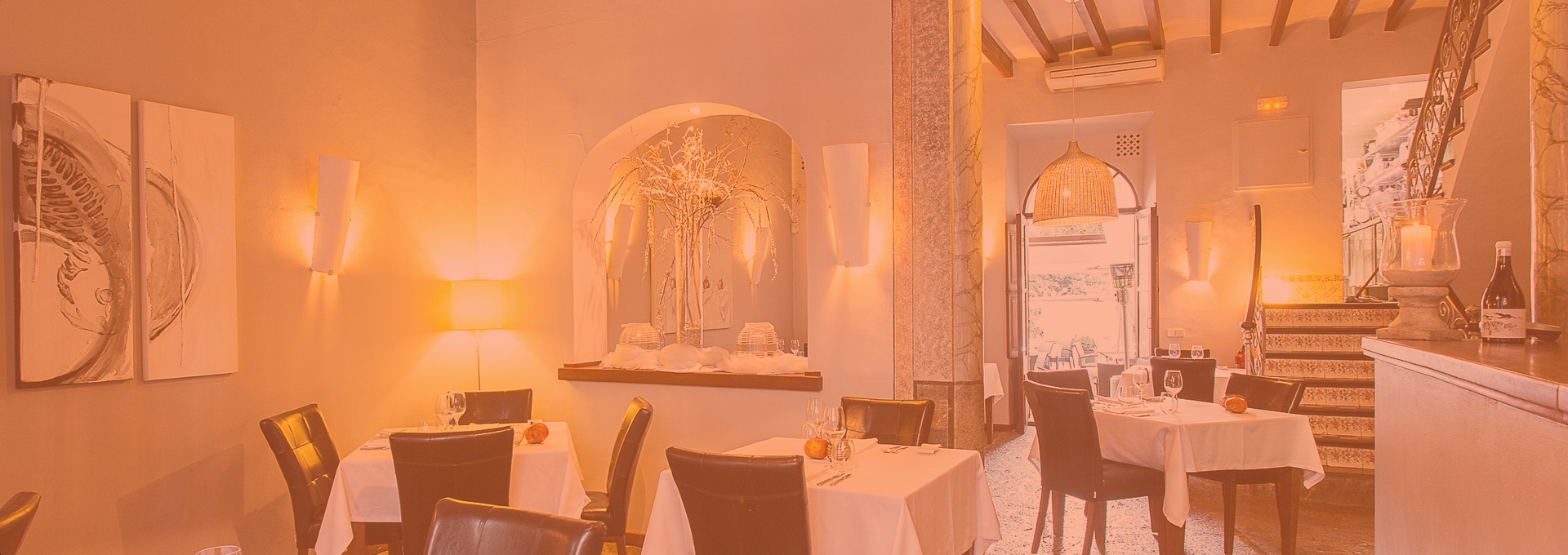 Ca'n Boqueta (Sóller): Bib Gourmand aan de Gran Via 3 De zaal van Ca'n Boqueta bij avond, met gedekte tafels onder houten balken en warm licht tegen de witte muren